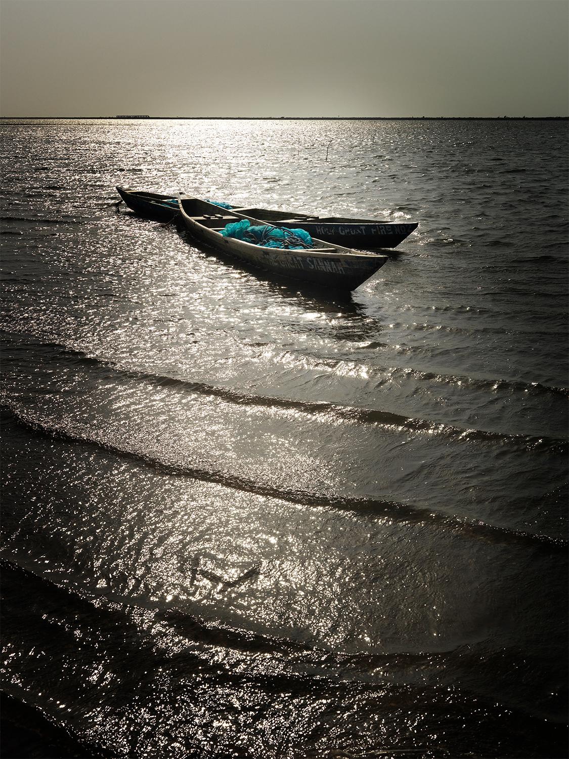 Edition of 25
signed and numbered by the artist

2 fishing boats drifting on the sea in Ghana. The water shimmers golden in the sunset.

JJK is a pseudonym for one of the world's most successful photo artists.
In his series "Always in my mind", he