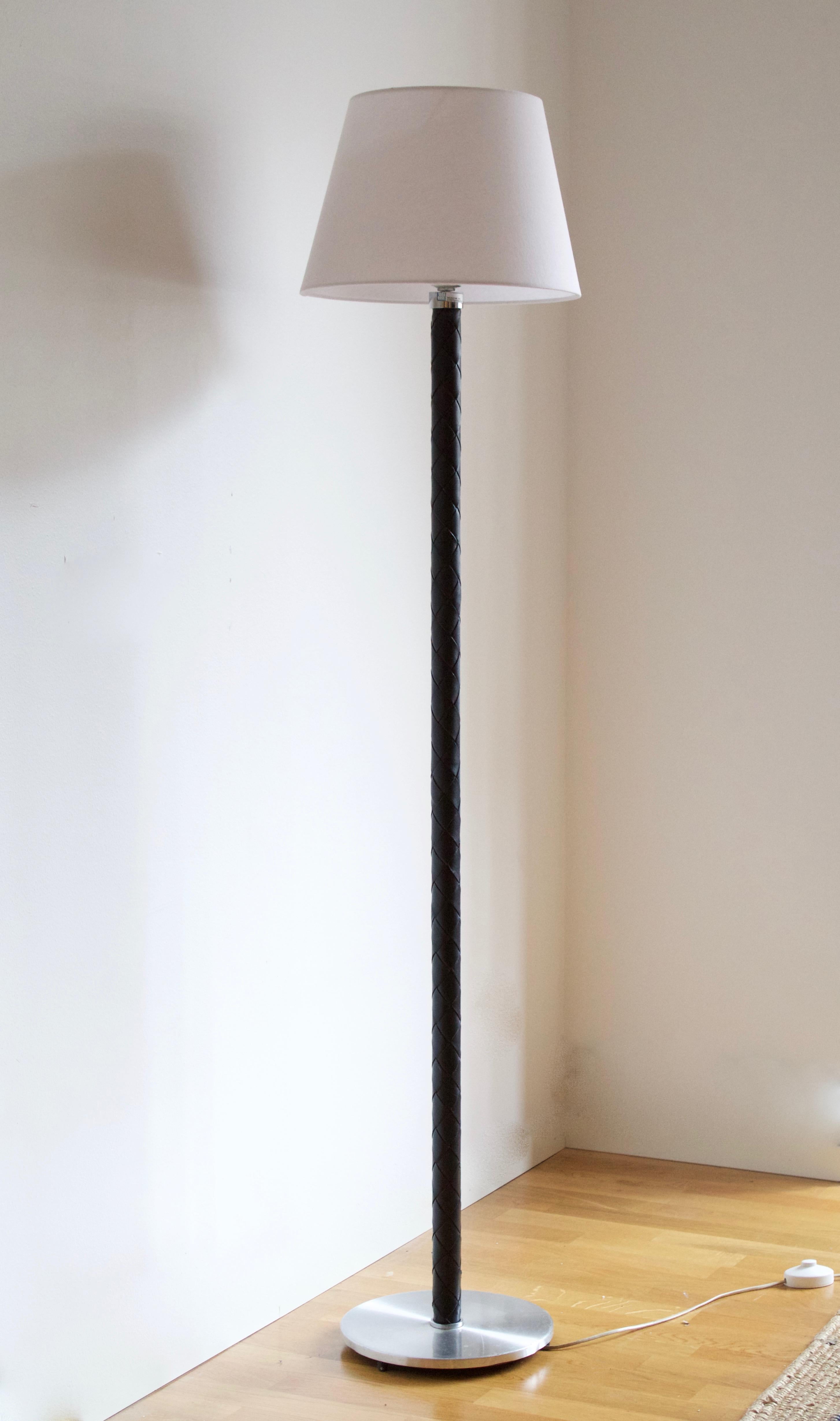 A Danish modernist floor lamp designed by Jo Hammerborg for Fog & Mørup. Base of stainless steel, rod covered in braided black dyed leather. Labeled

Stated dimensions exclude lampshade. Height includes the harp. Sold without