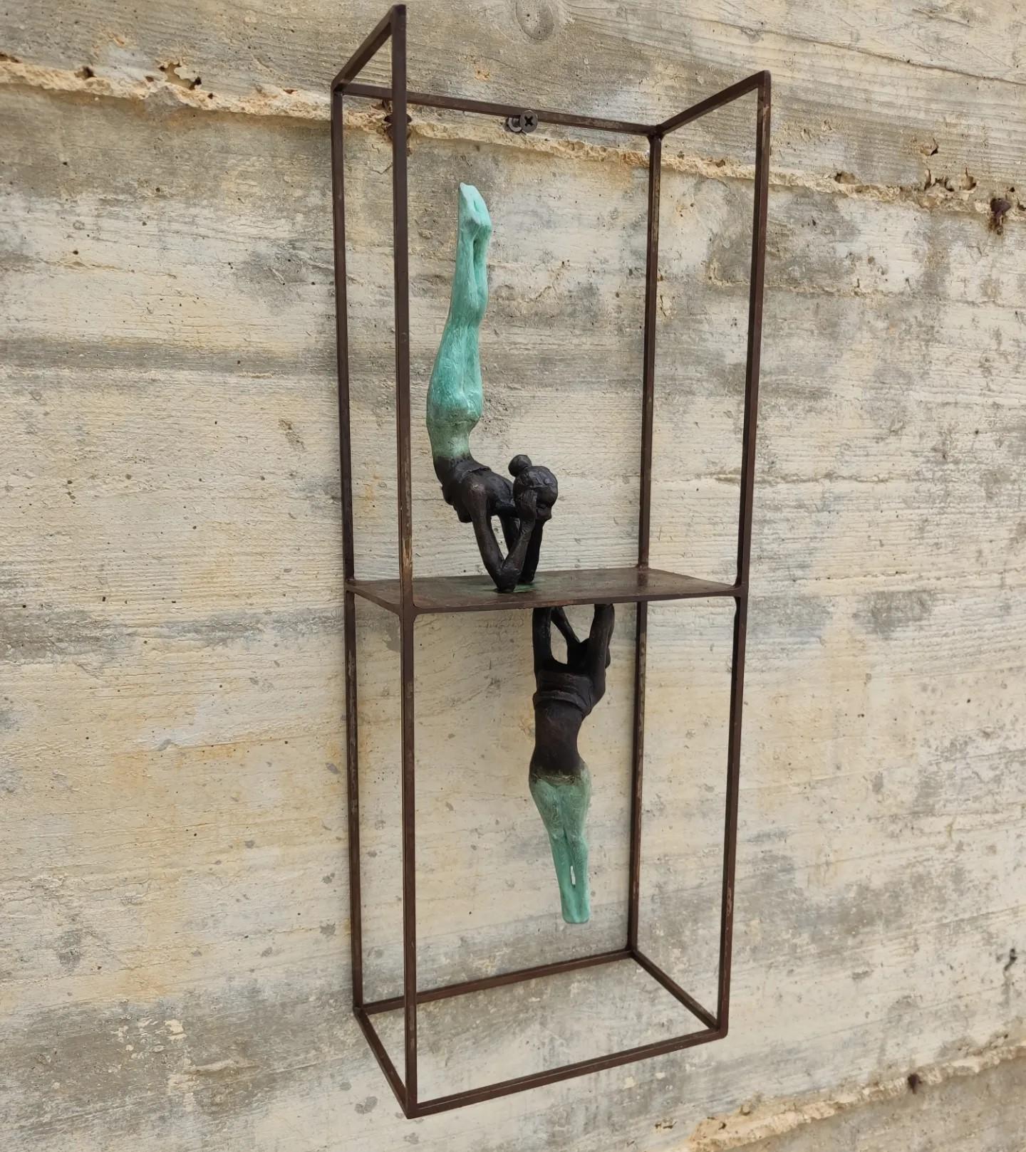Reflex ist eine Wandtischskulptur aus Bronze, die mit einem Stahlsockel verbunden ist. Die Skulptur zeigt menschliche Figuren in einer dynamischen Pose, als wären sie mitten in der Bewegung. Die fließenden Linien der Skulptur vermitteln den Eindruck