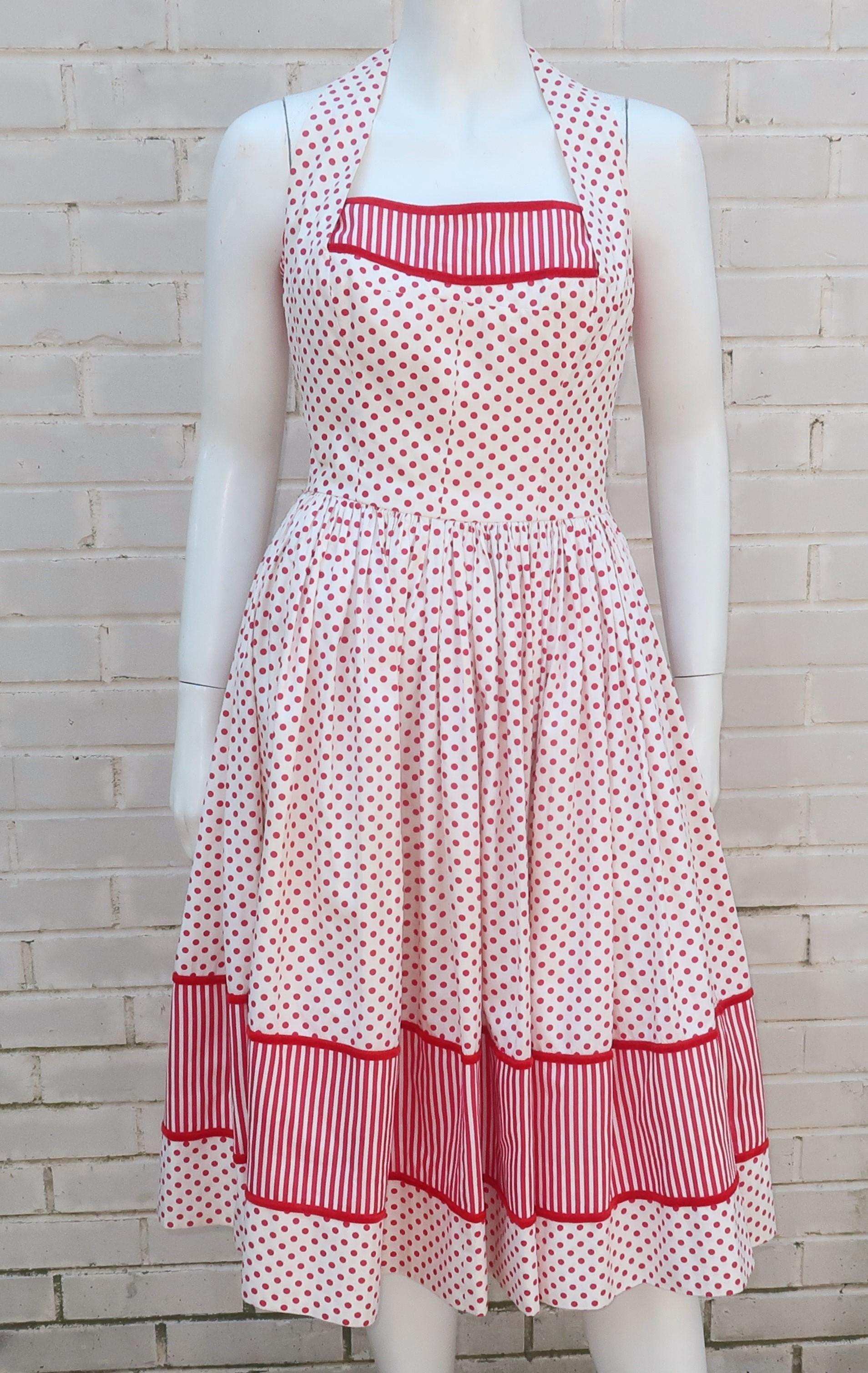 Holen Sie sich den amerikanischen Pin-up-Girl-Look mit einem Joan Barrie-Trägerkleid aus den 1950er Jahren in einem rot-weiß gepunkteten Baumwollstoff mit gestreiften Akzenten und rotem Samtbesatz.  Der Neckholder-Ausschnitt wird am Rücken geknöpft