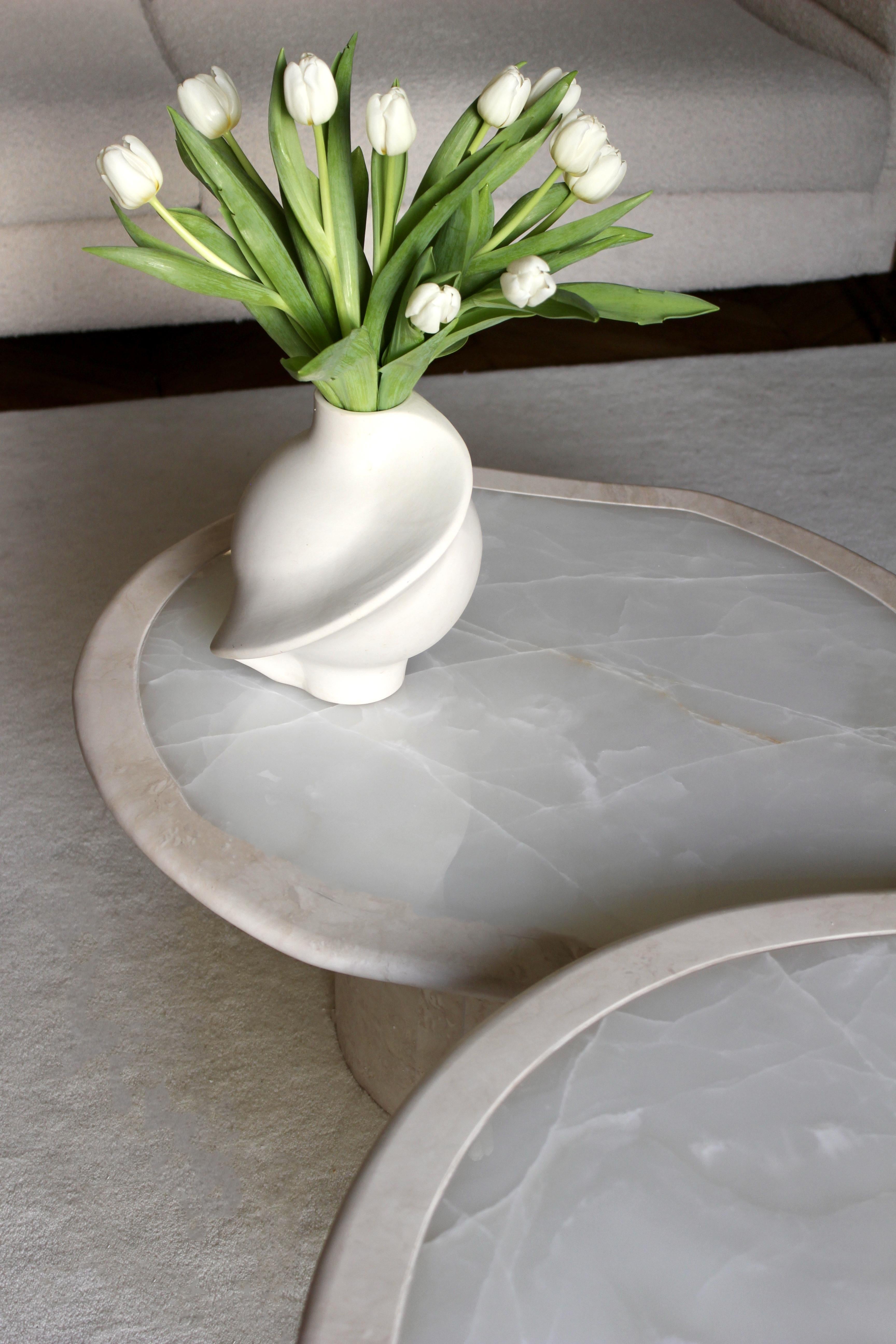 La table basse Whiting est définie par deux plateaux de forme organique avec un mélange de travertin et d'onyx blanc. Les bases rondes sont en travertin. Le design a été conçu pour être élégant, sophistiqué et visuellement fluide. Ces tables sont de