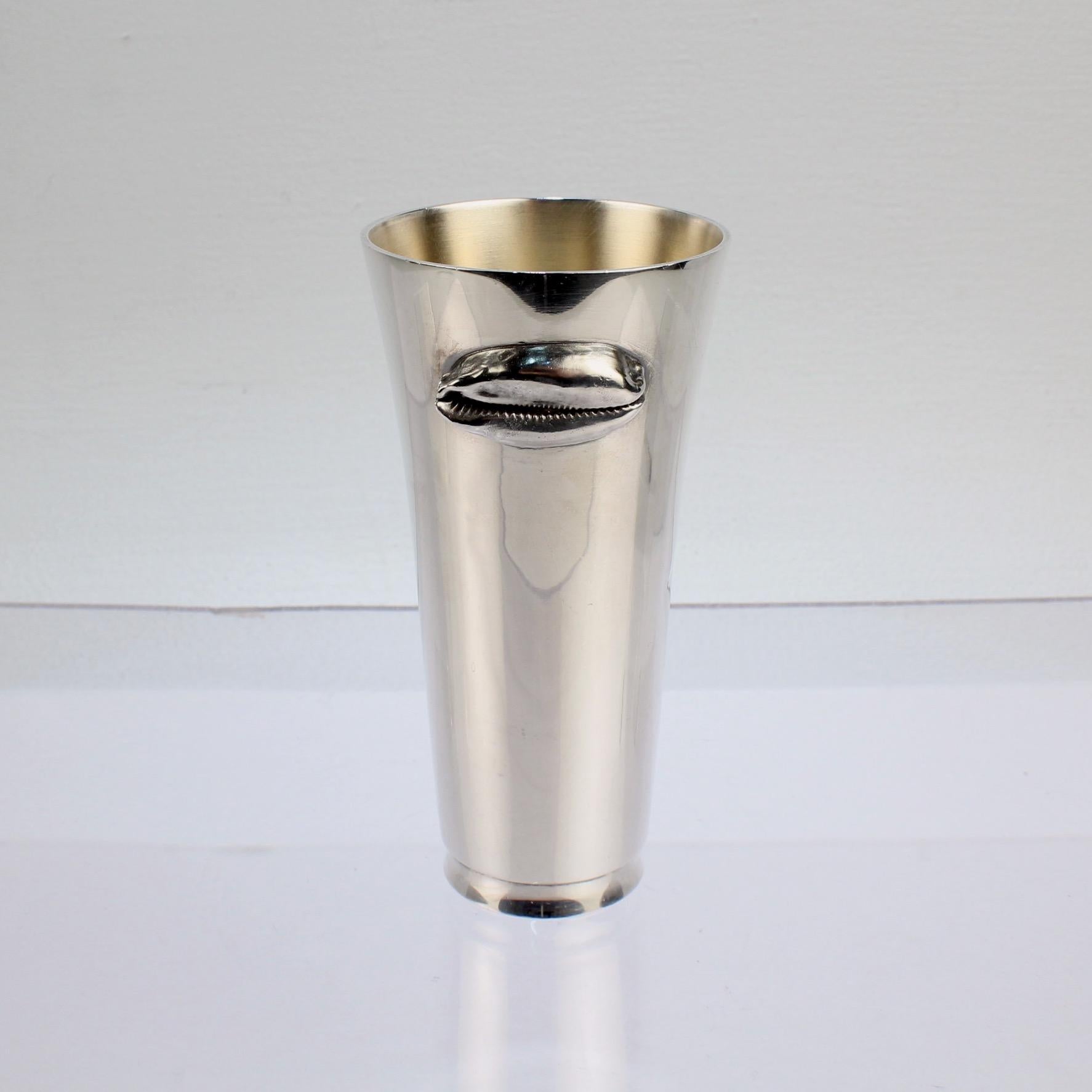 A wonderful tumbler or cup by Jocelyn Burton.

In sterling silver with an applied figural cowrie shell, tapered sides and gilt interior.

Jocelyn Burton was an enormously important English female silvermith and goldsmith. She executed numerous