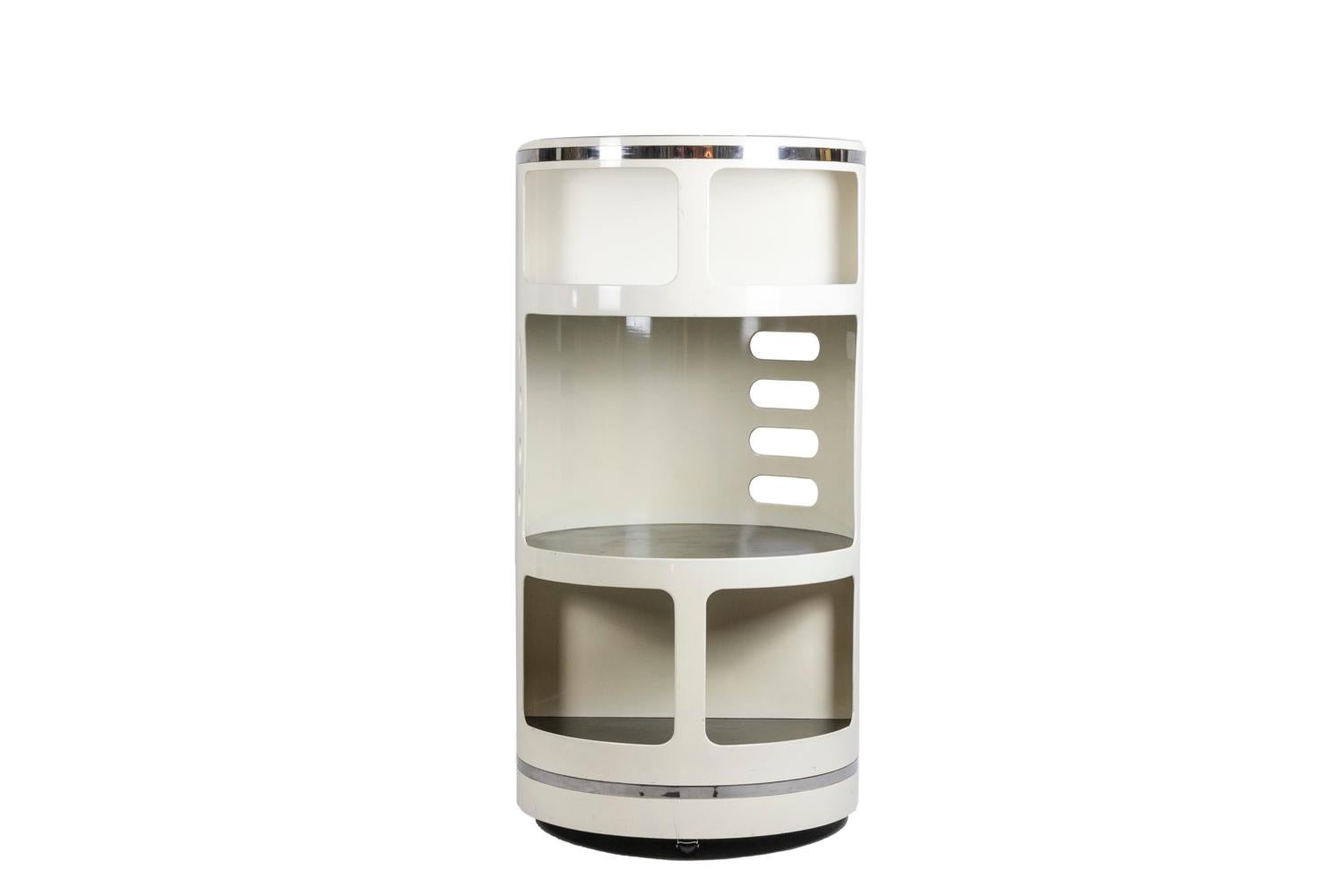 Joe Colombo, in the style of.

Cylindrical white plastic bar, with decorative openwork on the back and standing on wheels. Shelves in black leather. Finishes in chromed metal in the lower part and in the upper part. A transparent window in the