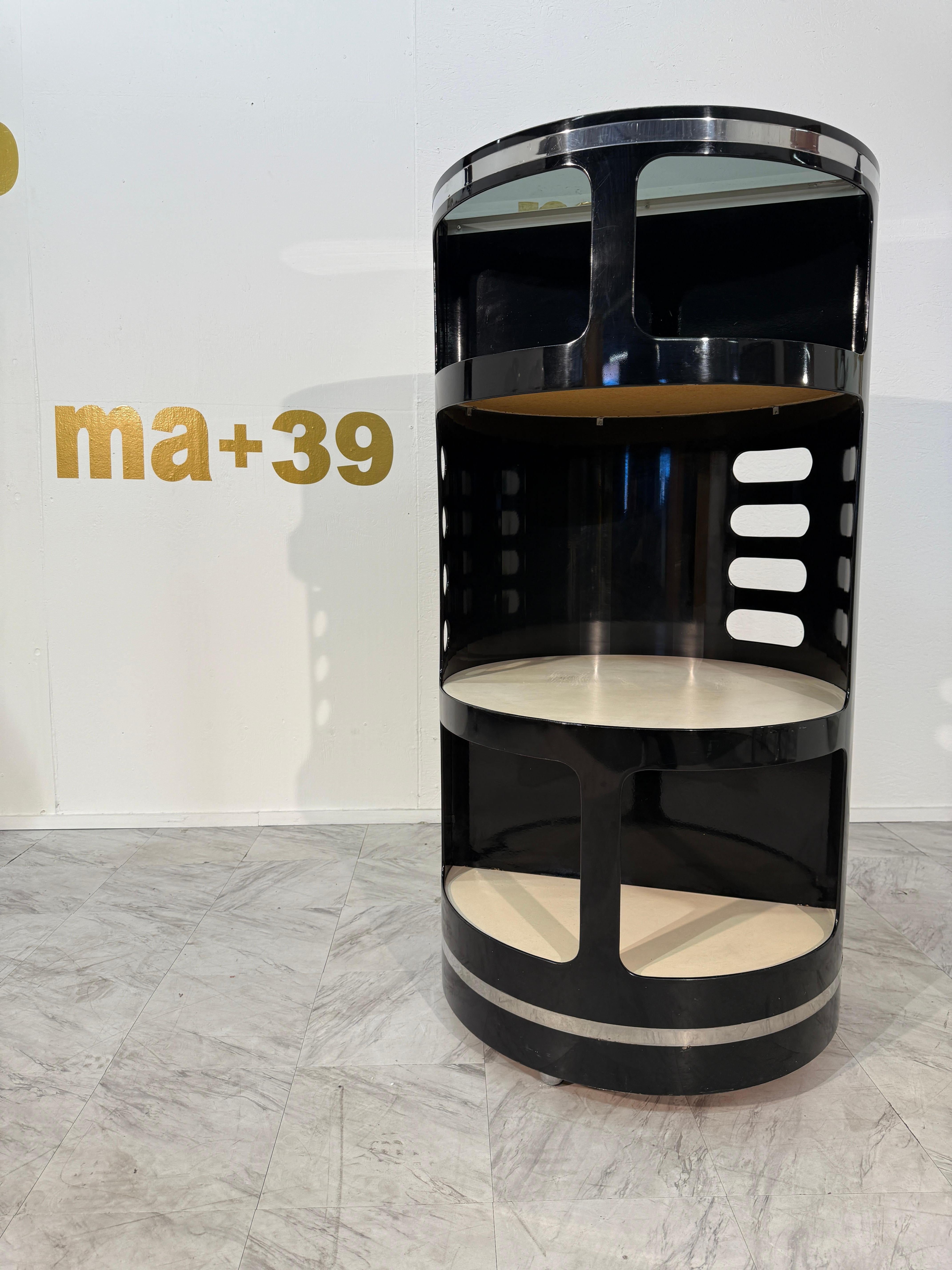 This cylindrical dry bar is a bold example of futuristic Italian design from the 1970s by visionary Joe Colombo. Crafted in high-gloss black lacquer with polished chrome accents, it features a sculptural silhouette with open shelving and integrated