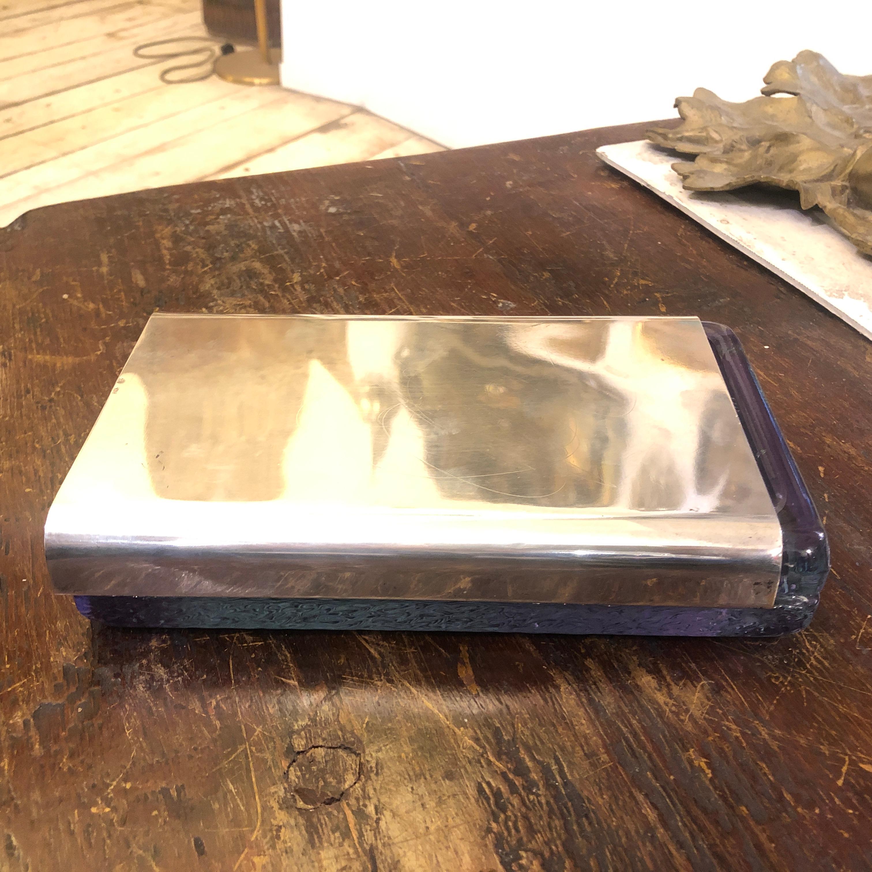 It's a crystal and silver cigarette box designed by Joe Colombo for Arnolfo di Cambio, it's a particular glass that change color with different light, Good conditions overall. There are two versions of this box, this one has a 800/1000 solid silver