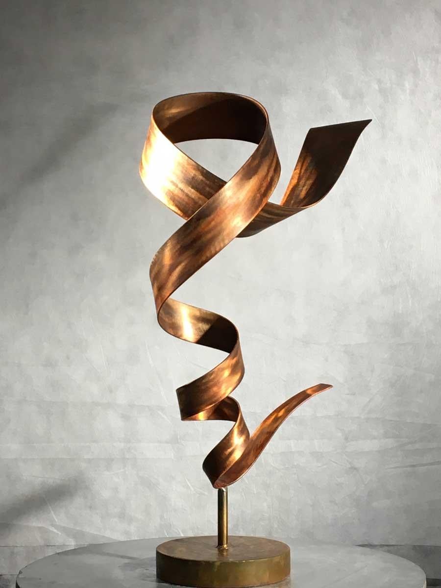 Questa scultura astratta contemporanea di medie dimensioni di Joe Sorge è realizzata in acciaio, tintura arancione e cera. Questo pezzo dai toni caldi è caratterizzato da una striscia di metallo d'acciaio che si attorciglia e gira in un movimento