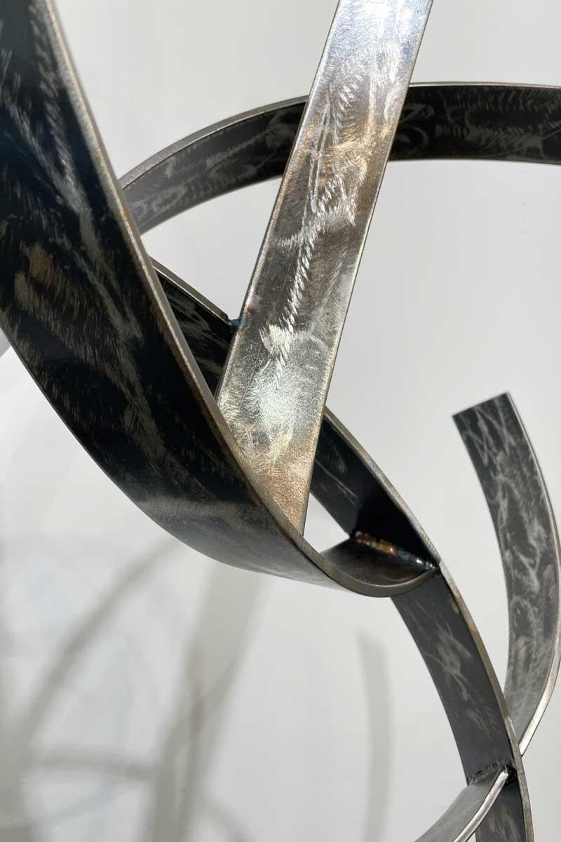 This large abstract contemporary sculpture by Joe Sorge is made with carbon steel with a clear coat. The artist has combined curved strips of steel, which curve around one another and upward, creating a beautiful sense of movement and depth. The