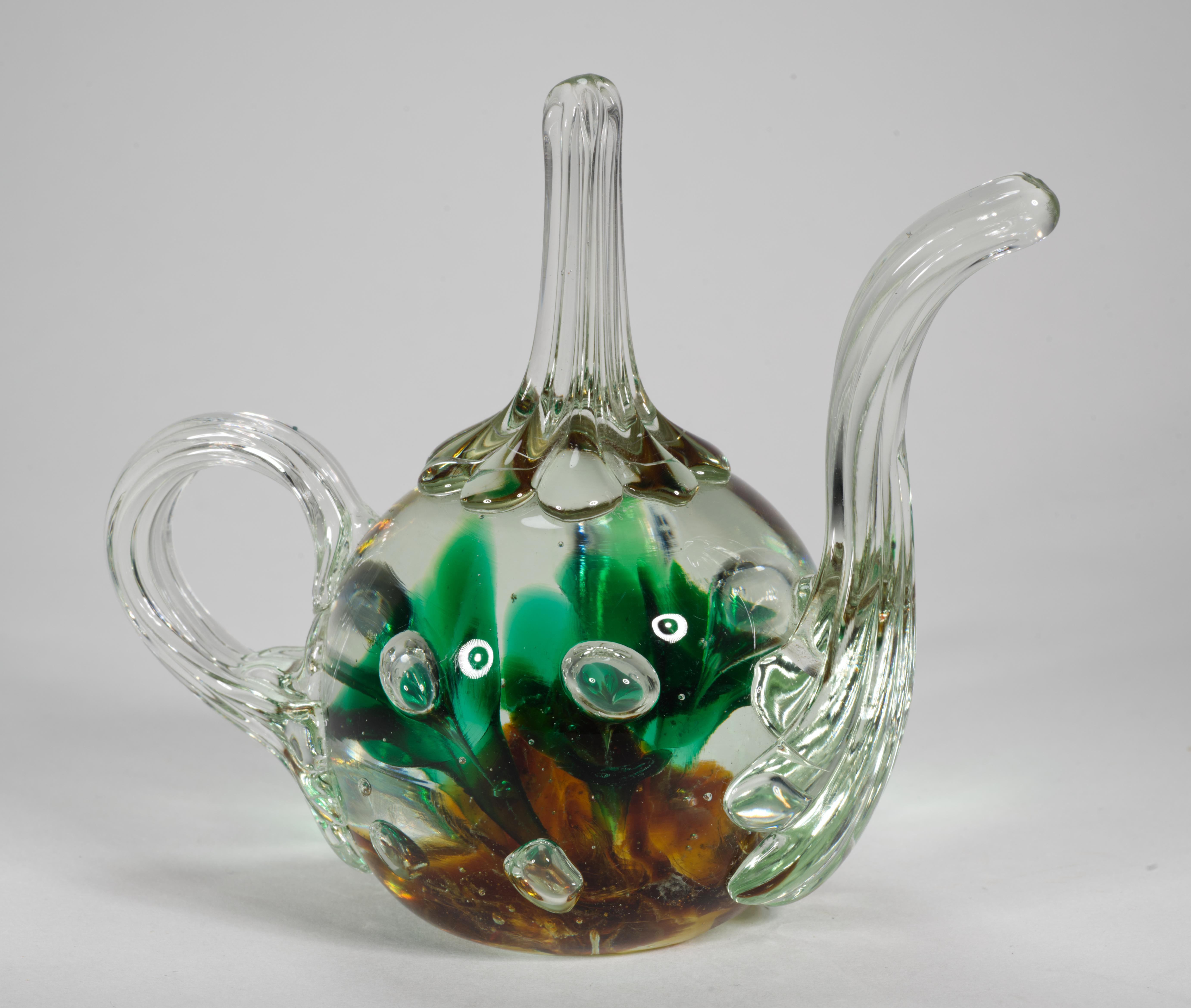  Large Joe St. Clair teapot shaped figural paperweight was intended for use as a ring holder, as well as a decor piece.  It features trumpet flowers in amber and forest green colored glass that are encased inside clear glass; there is a carefully