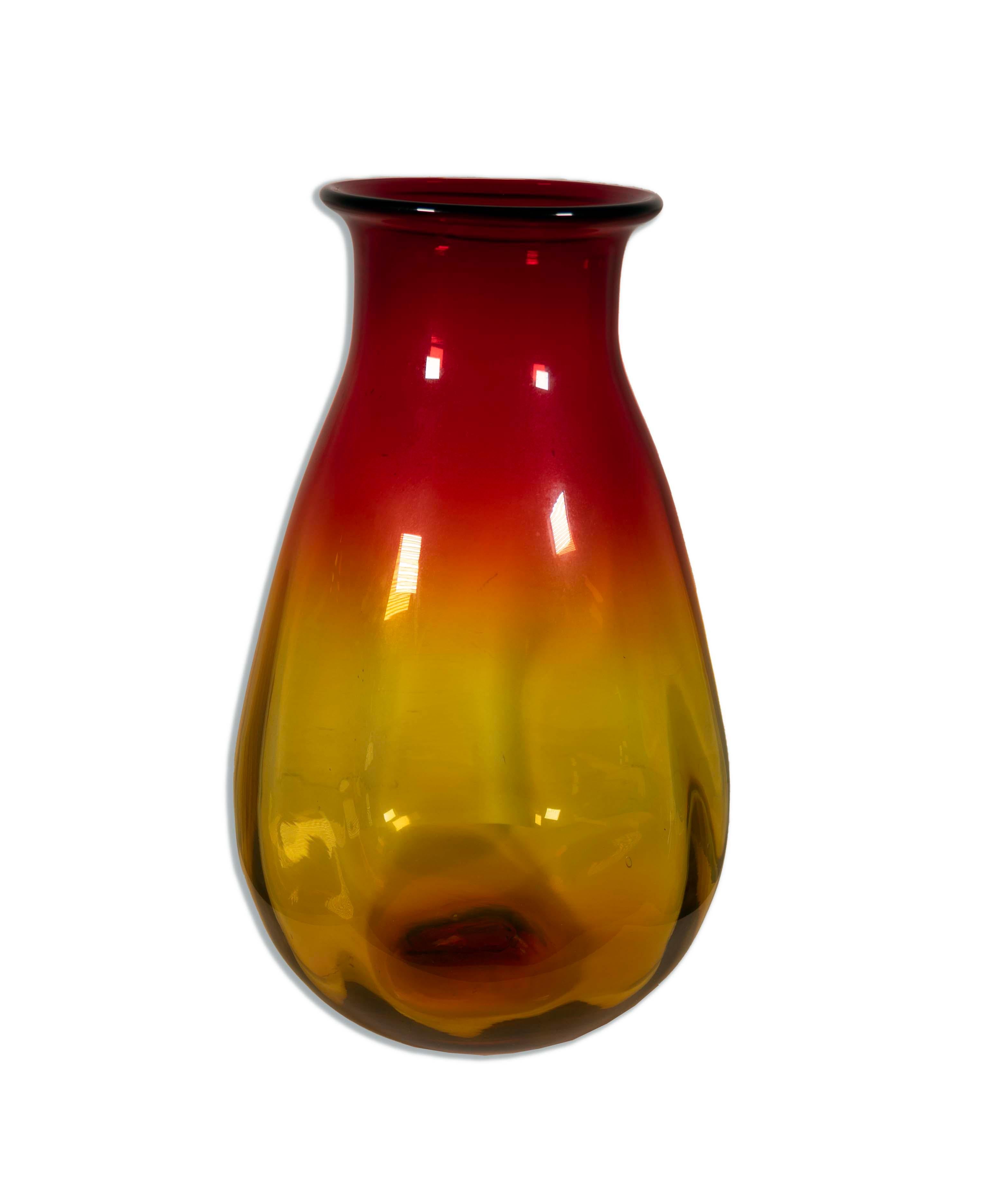 The Joel Myers for Blenko Red and Yellow Glass Vase, Model 7029, is a remarkable piece of mid-century modern glass artistry. Crafted by Joel Myers and the renowned Blenko Glass Company, this vase features a captivating, curvaceous form in a