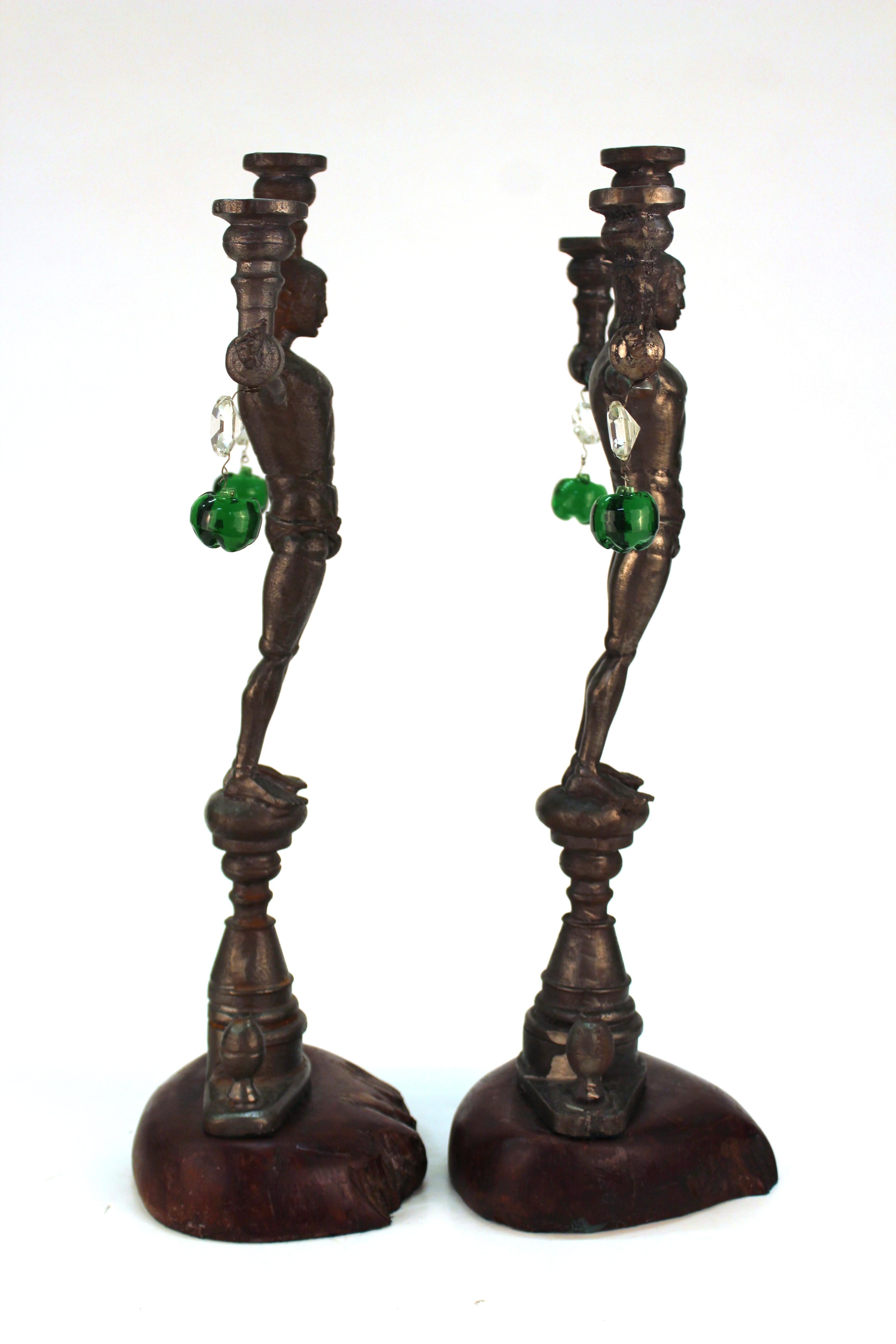 A pair of cast iron candelabras in the shape of G.I. Joe action figures in the nude with stretched out arms, created by California artist Joel Otterson (b. 1959) in circa 1992. The pair has hanging lead crystal elements and is affixed to wood bases.