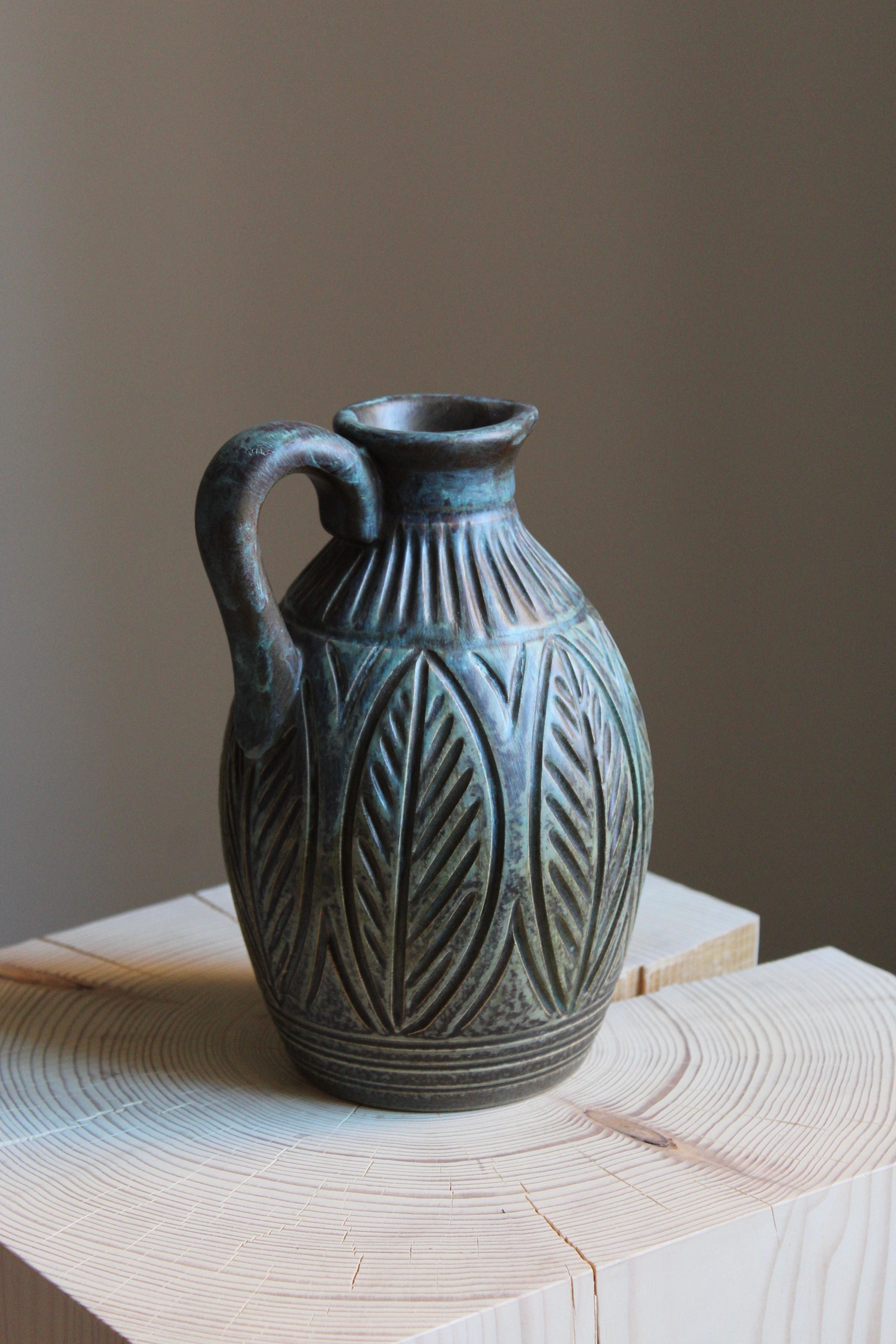 A finely ornamented and glazed stoneware pitcher or vase. In grey / blue with tones of green. Produced by Joghus Keramik, Bornholm, Denmark, 1956.

Other designers of the period include Axel Salto, Arne Bang, Wilhelm Kåge, and Stig Lindberg.