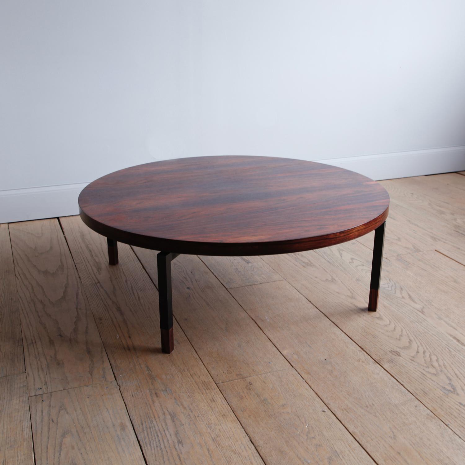 Minimalist design, maximalist materials. A large, low circular rosewood coffee table with sharply angled steel legs ending in solid rosewood feet.