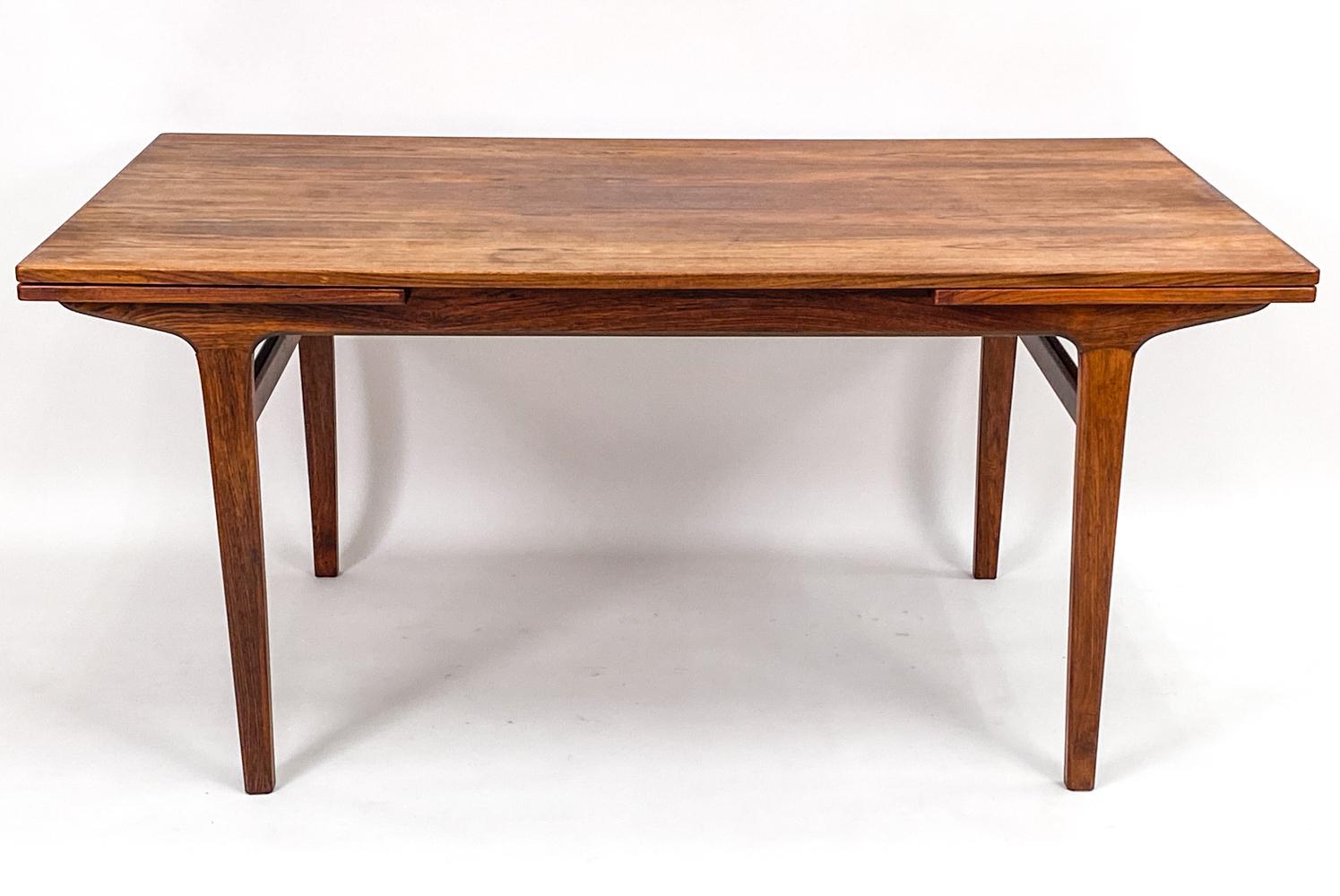 A gorgeous Danish mid-century dining table in stunning rosewood designed by Johannes Andersen. The minimalist design of this rectangular table lets the beautiful rosewood color and grain shine without distraction. Two hidden pull-out extension