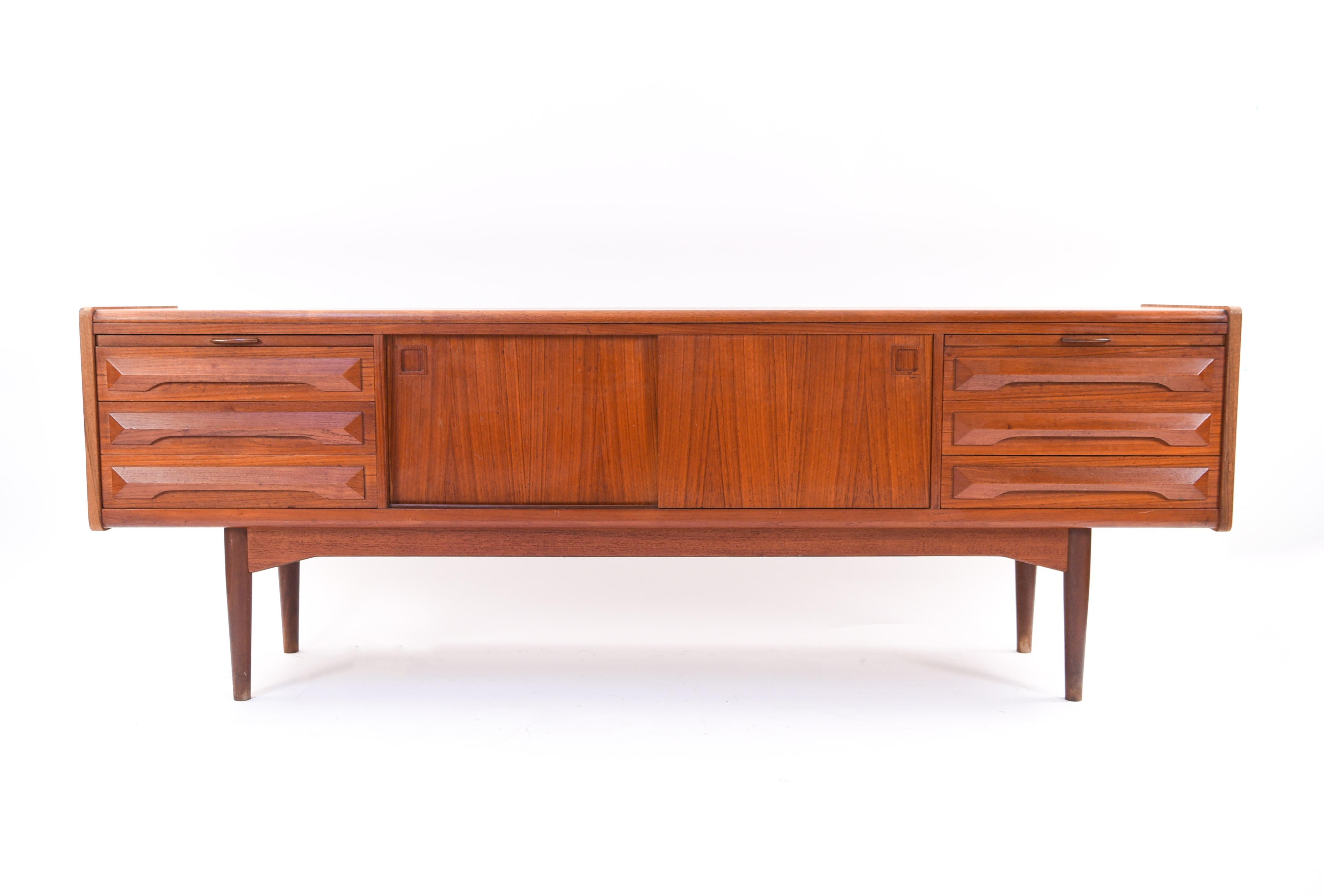 This interesting Danish midcentury teak sideboard was designed by Johannes Andersen in the 1960s and is attributed to Kofod-Larsen as the maker. This piece features the quintessential recessed square cabinet door handles of Andersen's design. The