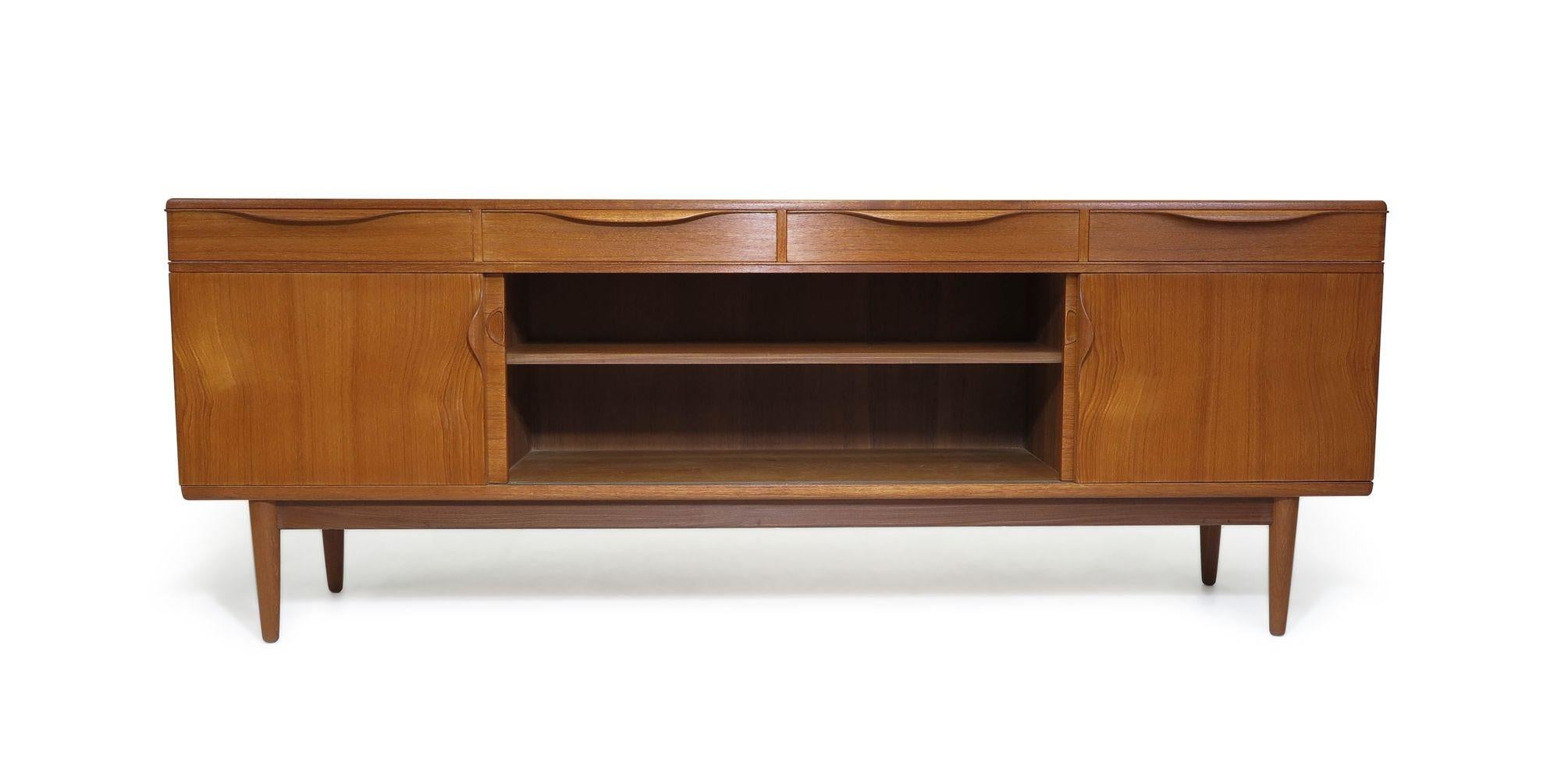 Mid-century teak credenza designed by Johannes Andersen, Denmark, 1960s. The sideboard is handcrafted of book-matched old-growth teak with four sliding cabinet doors below four drawers; each with sculptural pulls. The doors open to reveal an