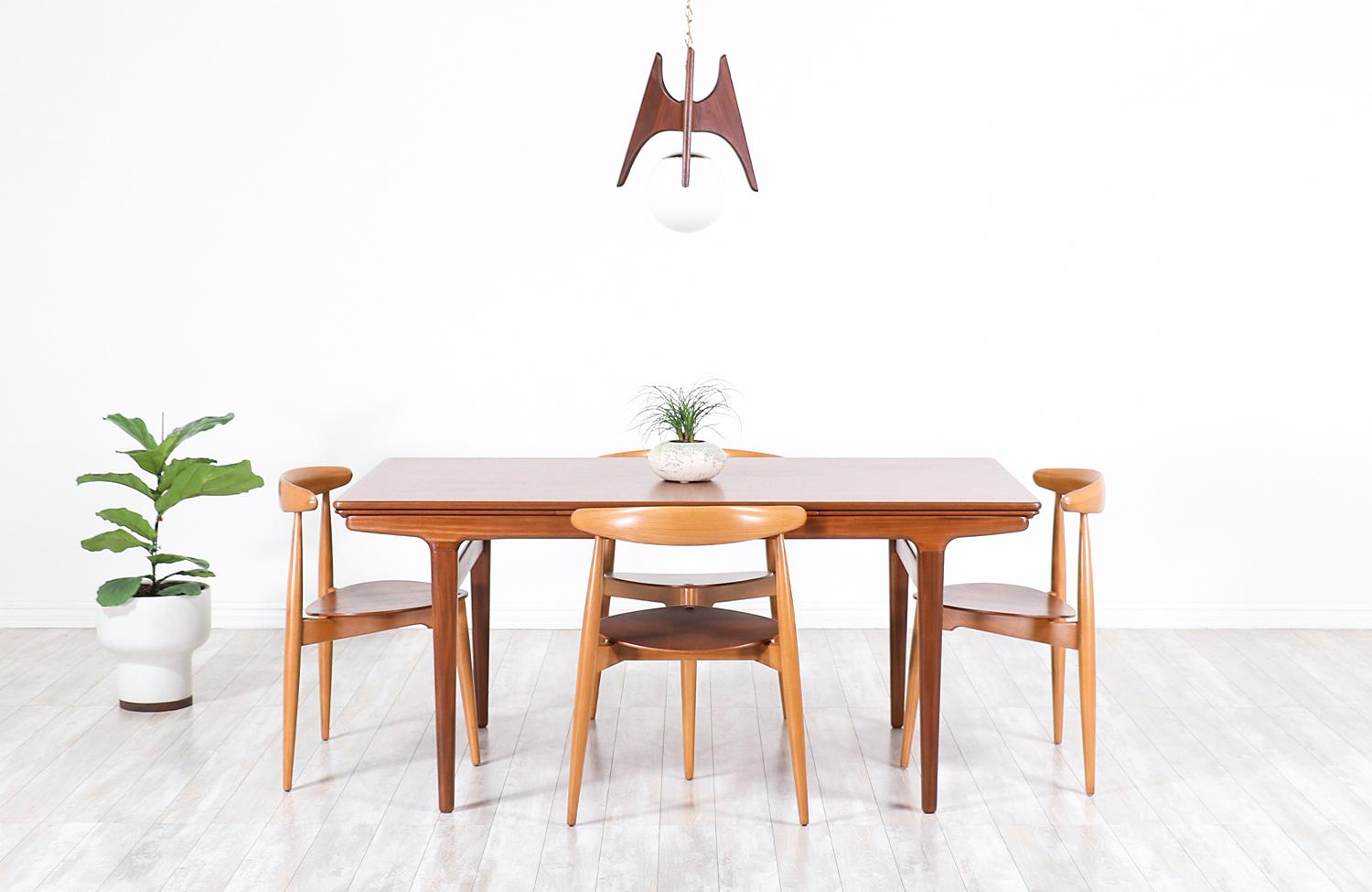 Stylish Danish modern draw-leaf dining table by Danish furniture designer Johannes Andersen and manufactured by Uldum Møbelfabrik, circa 1960s. This versatile table design features a solid teak wood body with a rectangular top and angled tapered