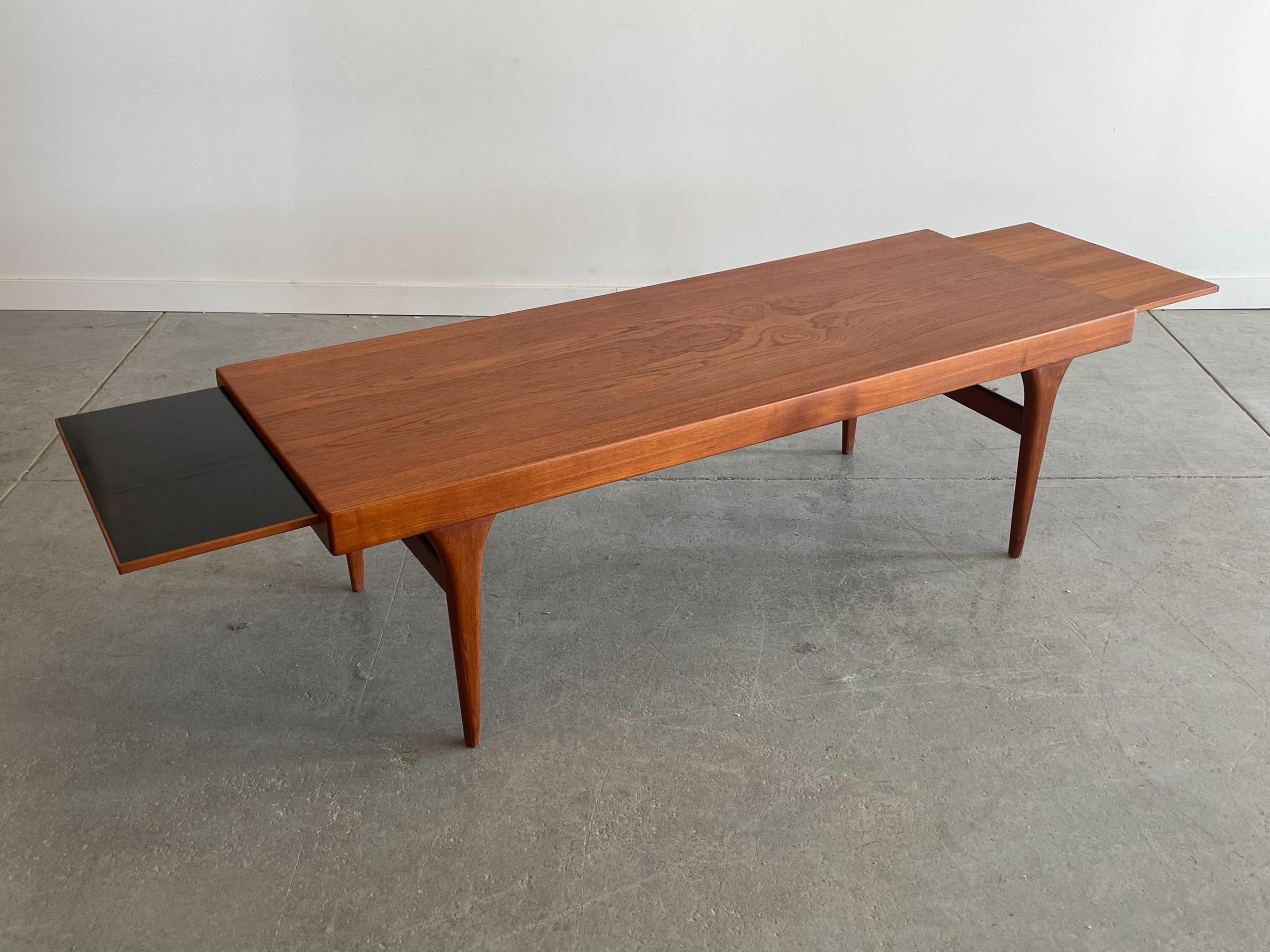 Stunning expanding teak coffee table designed by Johannes Andersen for CFC Silkeborg, Denmark. This piece features sculpted teak legs, a thick profile top, and nicely contoured pulls that reveal expanding surfaces (one laminated, one teak) either