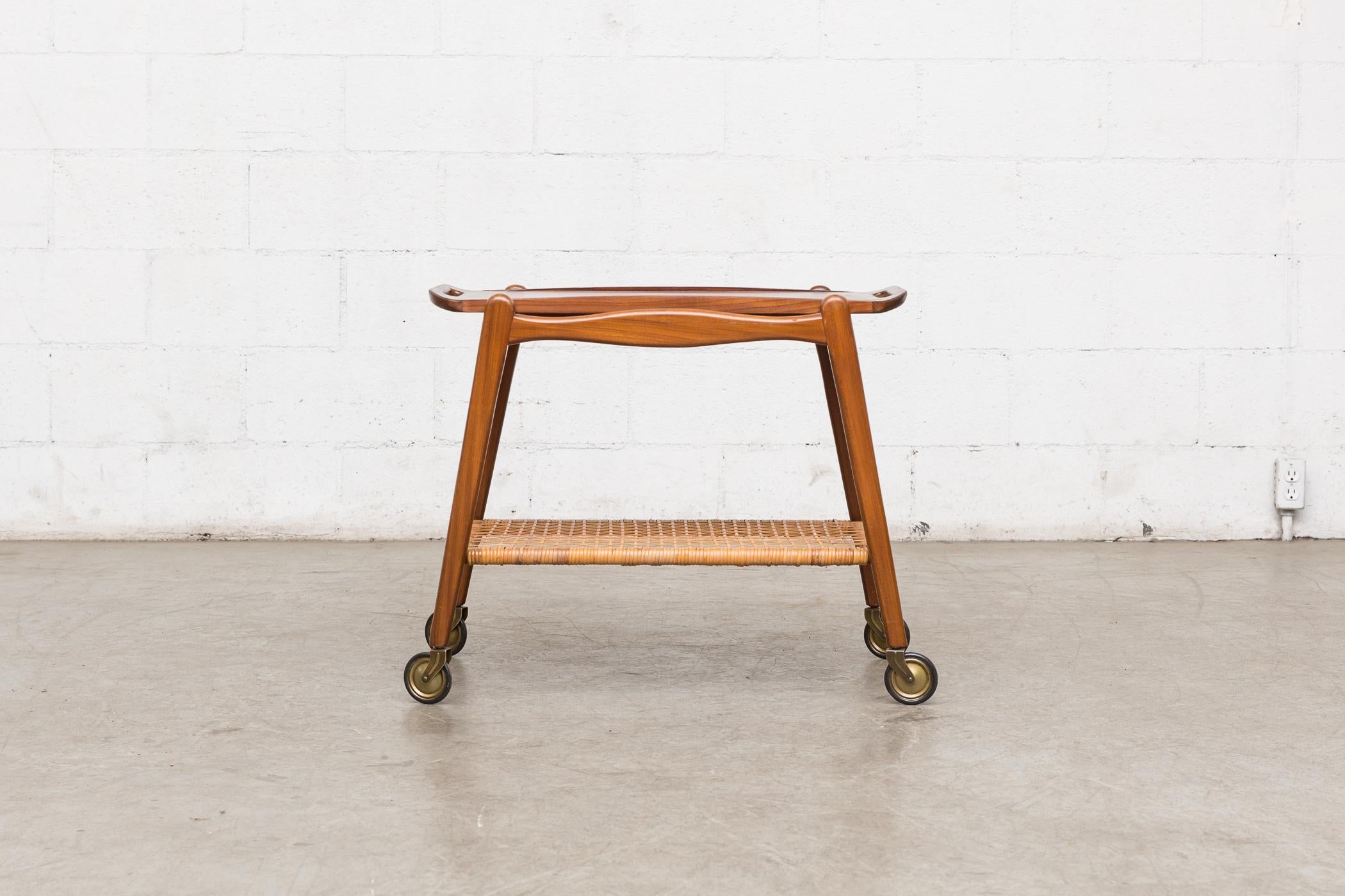 Mid-Century rolling cart by Johannes Andersen, Denmark. Lightly refinished teak. Removable tray with woven rattan lower shelf. In good original condition with some wear. Wear is consistent with its age and use. 2 available, with slightly varying