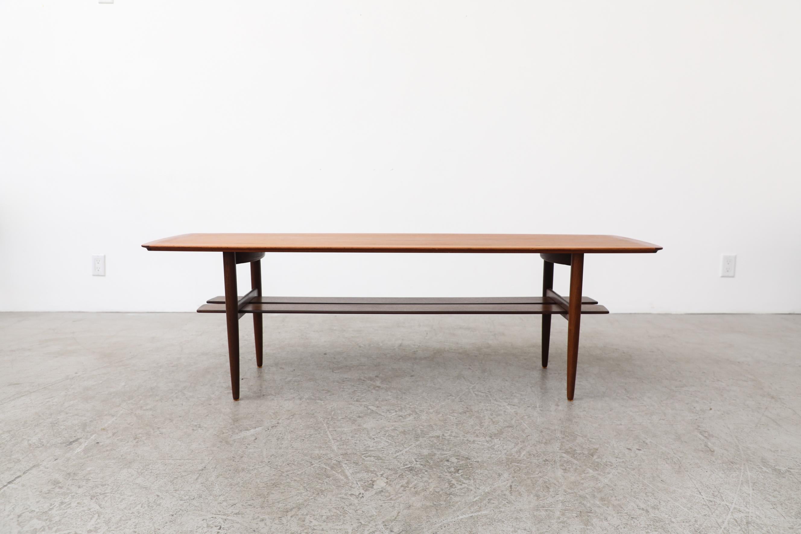Mid-Century modernist tall coffee table designed by Johannes Andersen with interesting split plank lower magazine shelf. Each side of the lower shelf has a darker stained banner around the edges. It's in original condition with visible wear