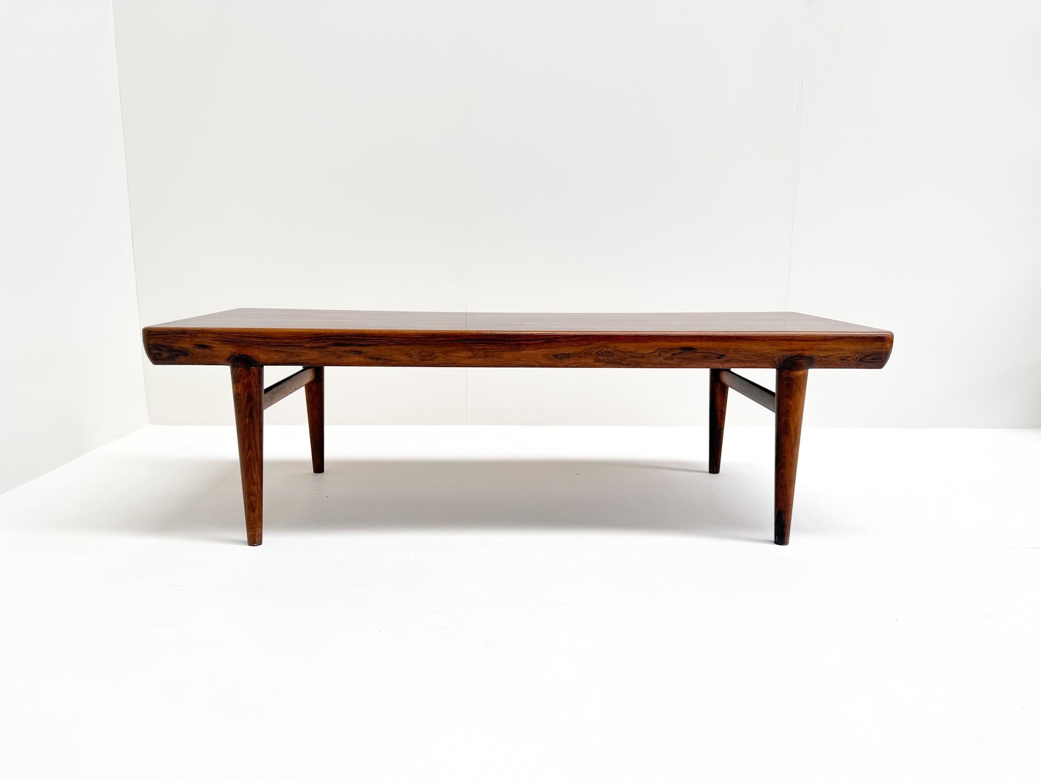 Esta impresionante mesa de centro de palisandro fue diseñada por Johannes Andersen para CFC Silkeborg en Dinamarca. Presenta una forma elegante y orgánica, con bordes suaves y redondeados y patas cónicas. El palisandro tiene un veteado rico y
