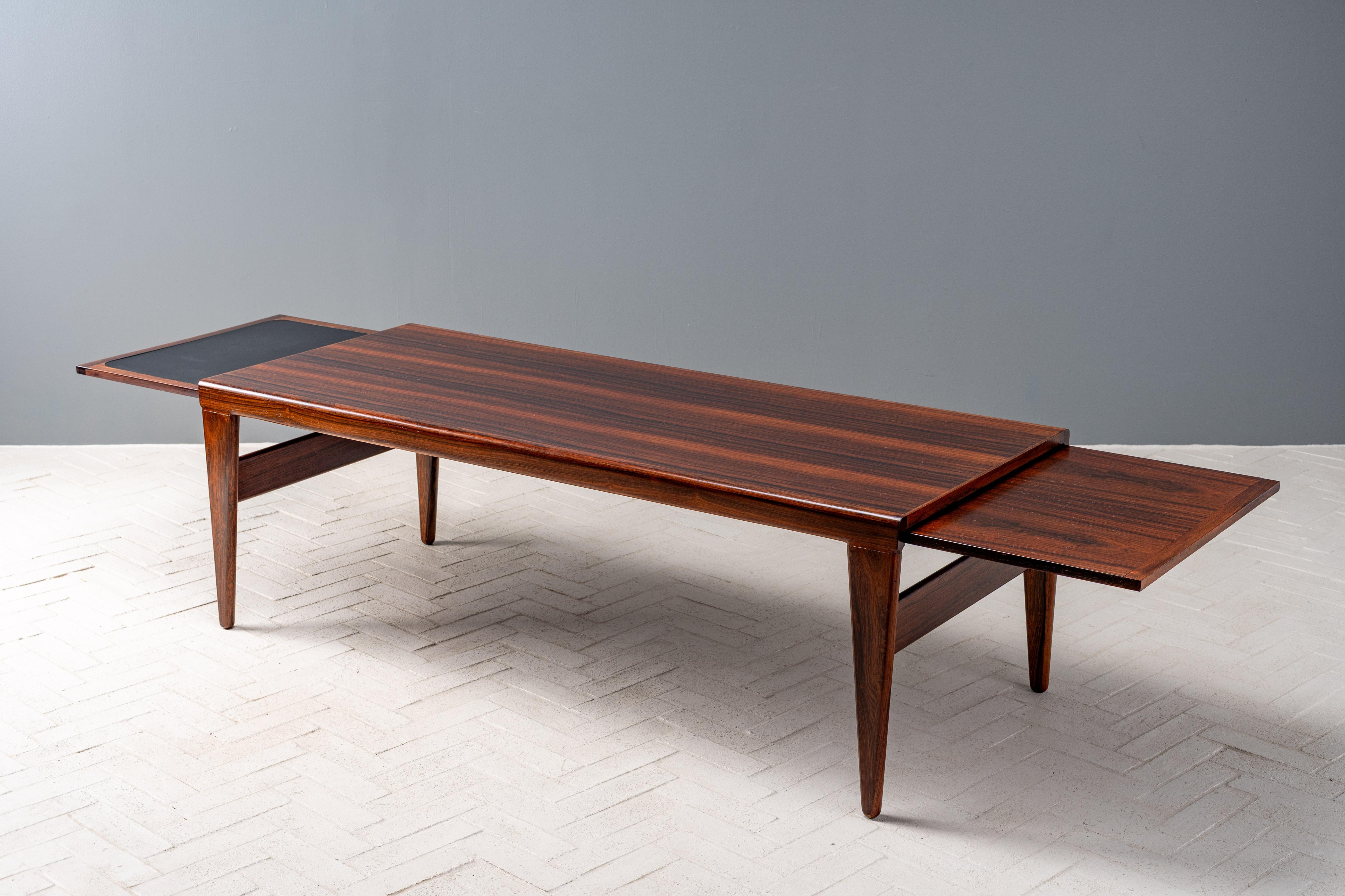 Denmark, ca. 1960s. An elegant yet substantial rosewood coffee table by Johannes Andersen. Features rosewood construction with a rectangular top supported by sturdy triangular legs reinforced with wide parallel stretchers. Clever self-storing leaves