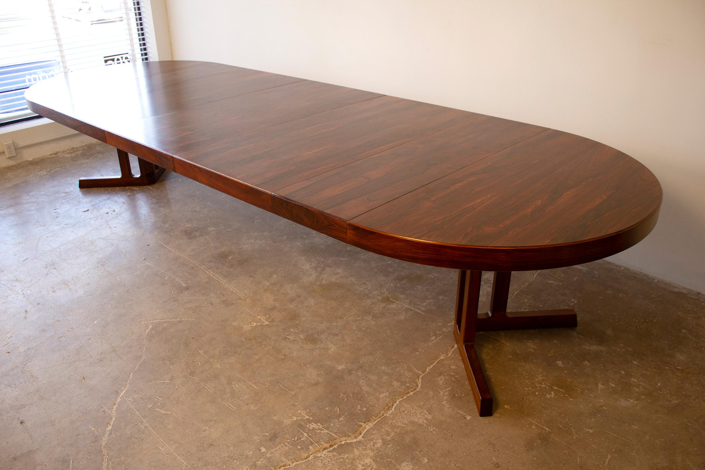 Massive Johannes Andersen Danish modern rosewood dining table fabricated in the 1960s. This table functions as a circular breakfast table but opens up to accept up to 5 leaves creating a massive banquet table that originally accommodated 14 highback