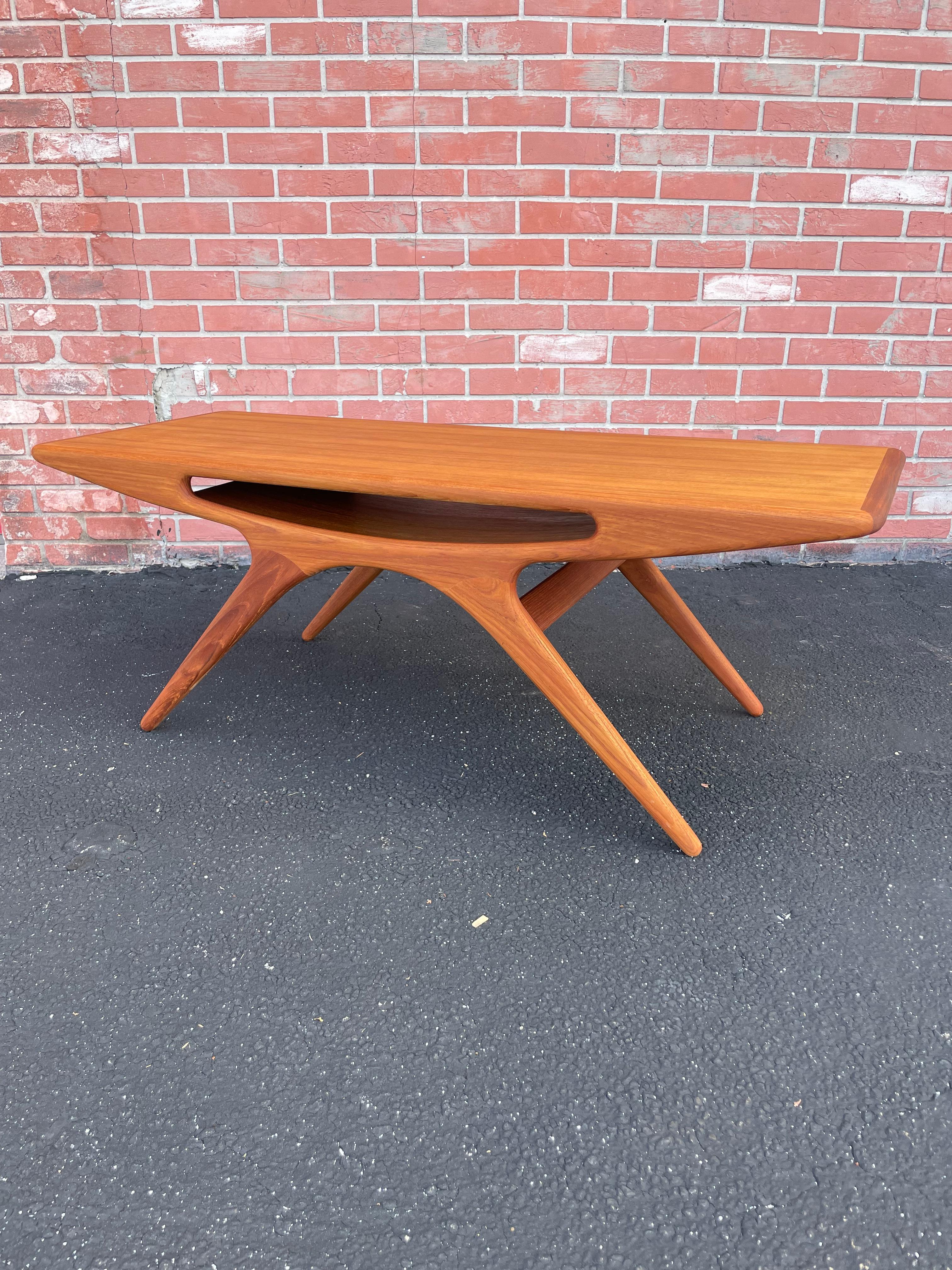 Iconic Smile Table by Johannes Andersen. Designed in 1957 for CFC Silkeborg in Denmark.  Slanted legs and a middle storage shelf with rounded edges.