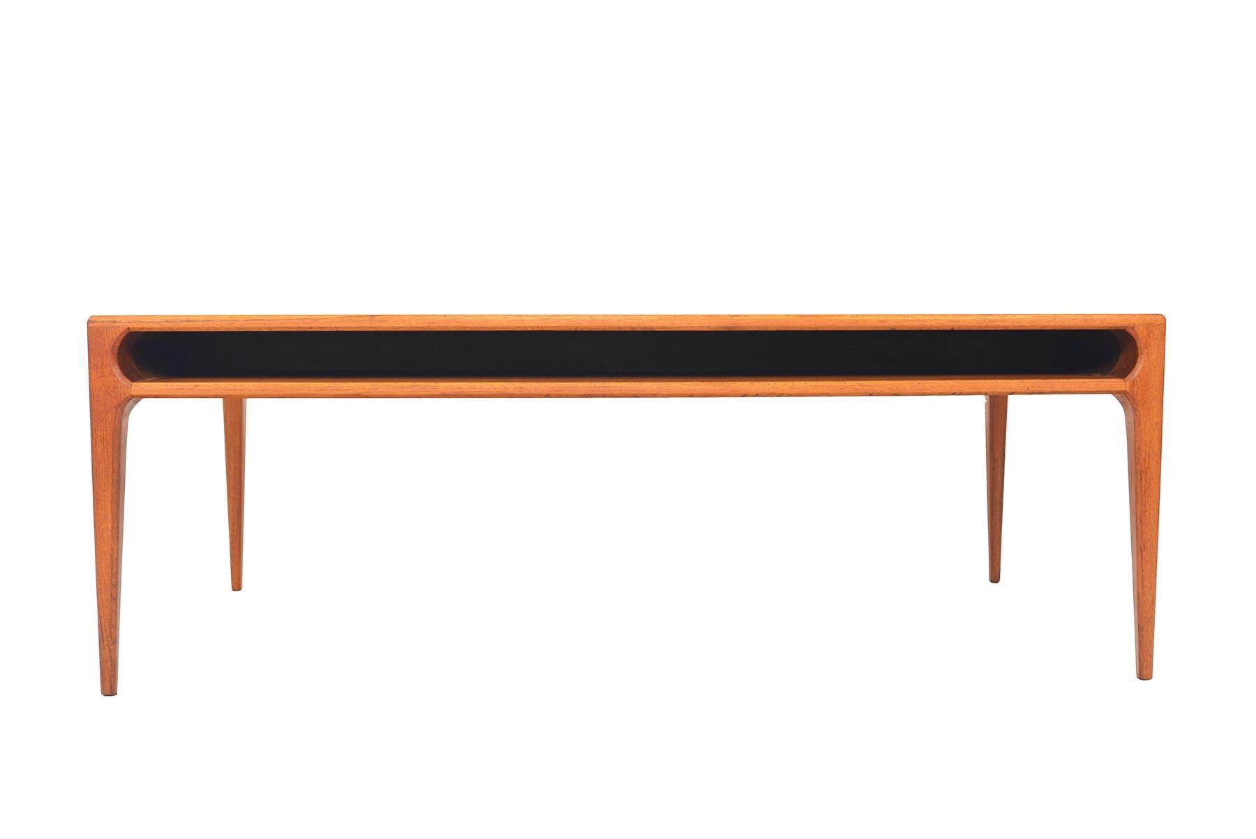 This Danish modern midcentury coffee table in teak was designed by Johannes Andersen in the 1960s. Expertly built, this gorgeous piece features solid teak legs which are seamlessly joined to the table top. The table offers a large cubby for storage.