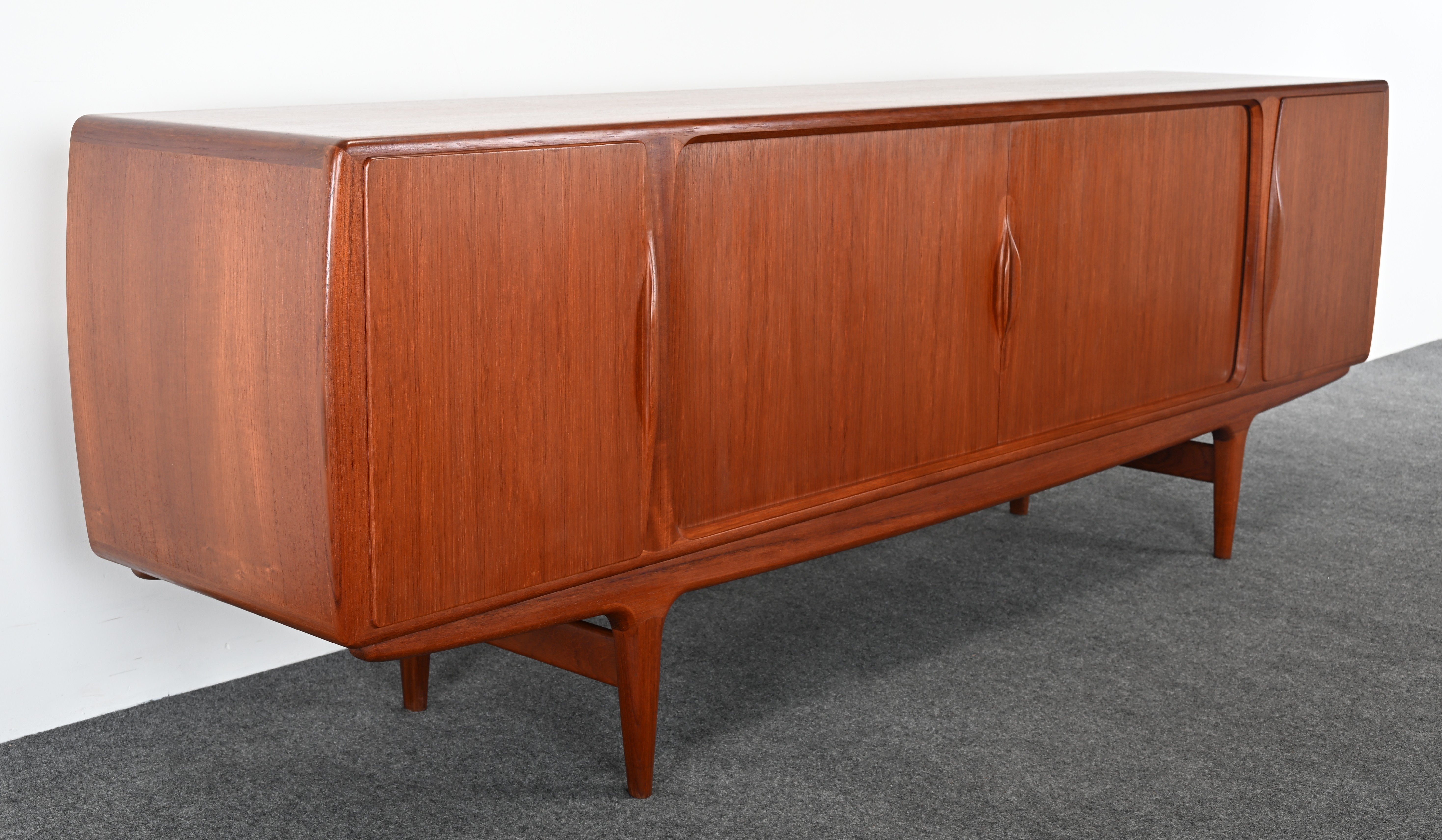 Impresionante aparador o credenza de teca de la modernidad de mediados de siglo, diseñado por Johannes Andersen, años 50. Uno de los mejores ejemplos de aparadores modernos escandinavos. Sus asas contorneadas y el detalle de la base le dan un