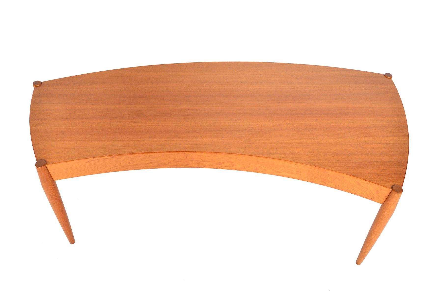 This Danish modern midcentury coffee table in teak was designed by Johannes Andersen for Trensum Møbelfabrik in the 1950s. Expertly built, this gorgeous piece features a sweeping curve teak tabletop and four sculpted legs. In excellent original