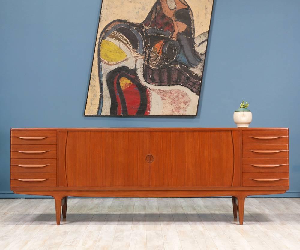 Skillfully crafted by Danish designer, Johannes Andersen, for Uldum Møbelfabrik in Denmark circa 1960, this lovely teak credenza features a flawless set of tambour doors, featuring recessed, semi-circle pulls, that smoothly glide open to reveal two