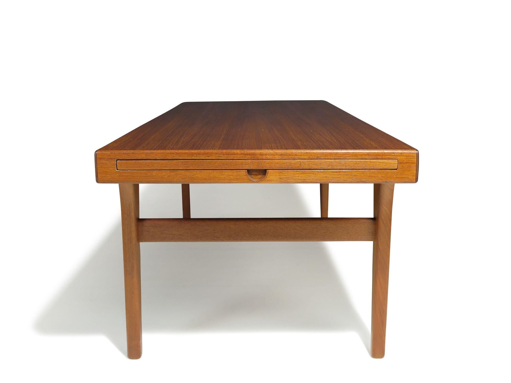 Designed by Johannes Andersen, this classic mid-century Danish coffee table is crafted from solid teak and features sturdy joinery throughout. Hidden pull-out trays on either end provide additional surface space, enhancing both form and function.The