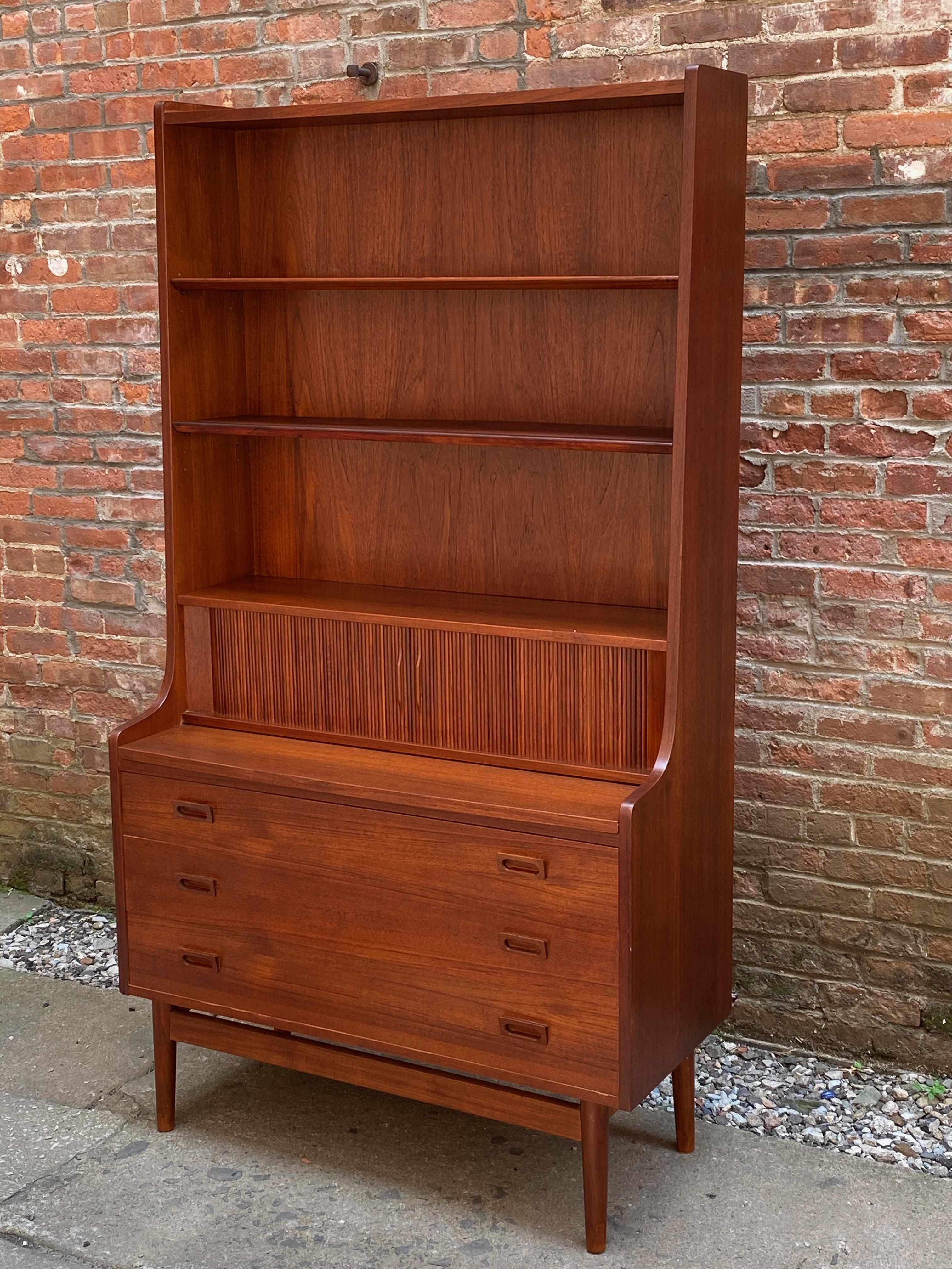 Johannes Sorth design for Bornholm Mobelfabrik teak desk/bookcase. Signed with paper label on the back. Nicely figured teak veneers on solid teak legs. Featuring two adjustable shelves, sliding desk top and two tambour doors over three drawers.