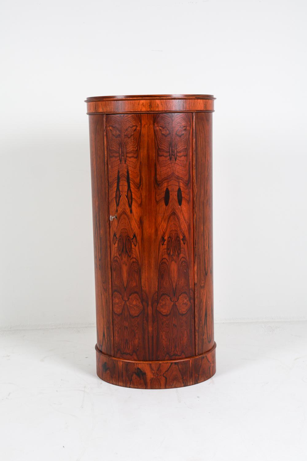 This cabinet is a rare and beautiful example of the Danish Modern style. Standing in a cylindrical/oval shaped pedestal, this cabinet is crafted from rosewood, with beautifully presented natural grains on full display. This particular model is