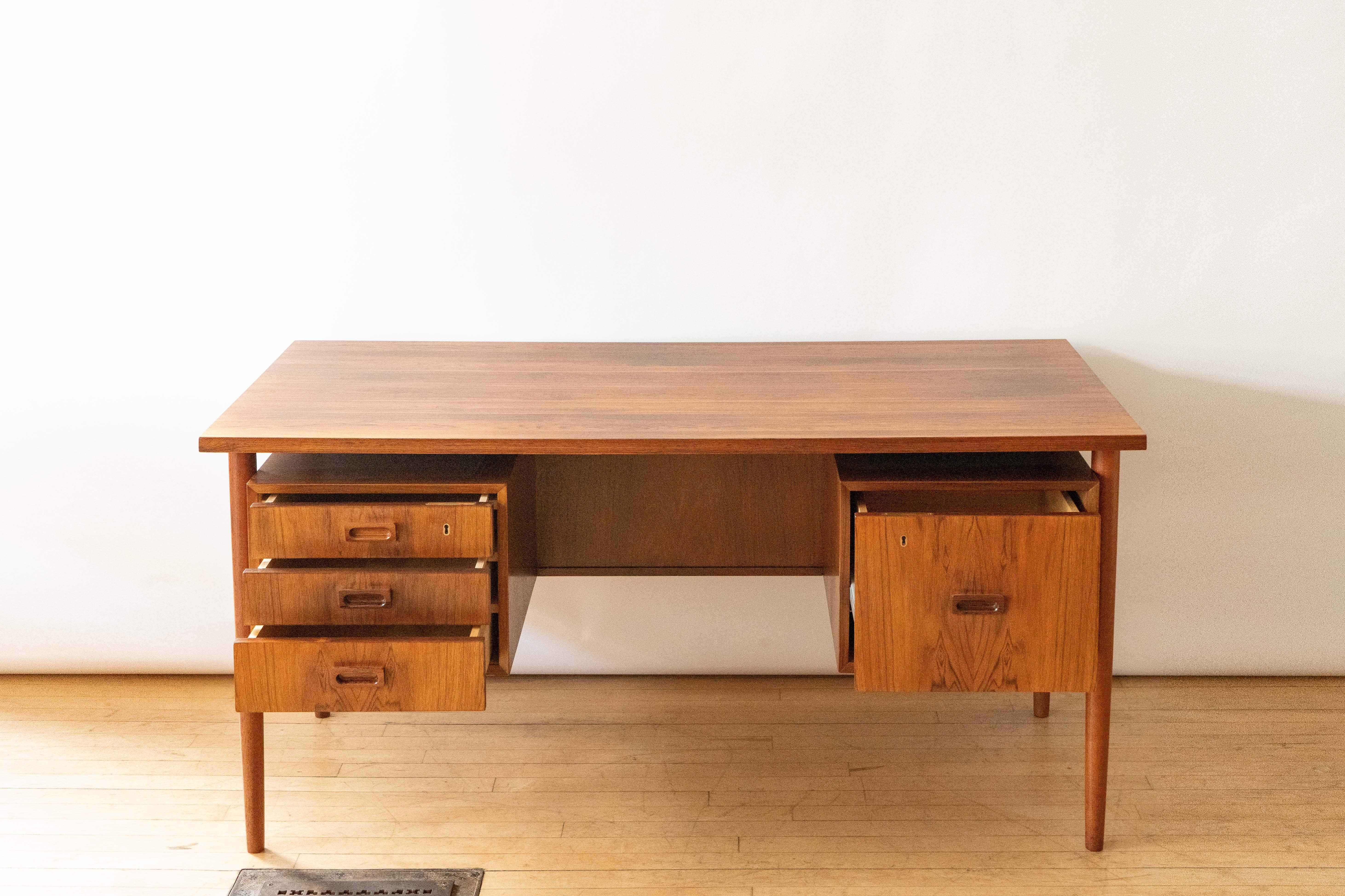 Denmark, ca. 1960s. An elegant executive desk by Johannes Sorth for Bornholm. Features richly grained rosewood construction with three medium drawers and one large drawer perfect for files. Carved rectangular pulls, tapered legs, and floating top