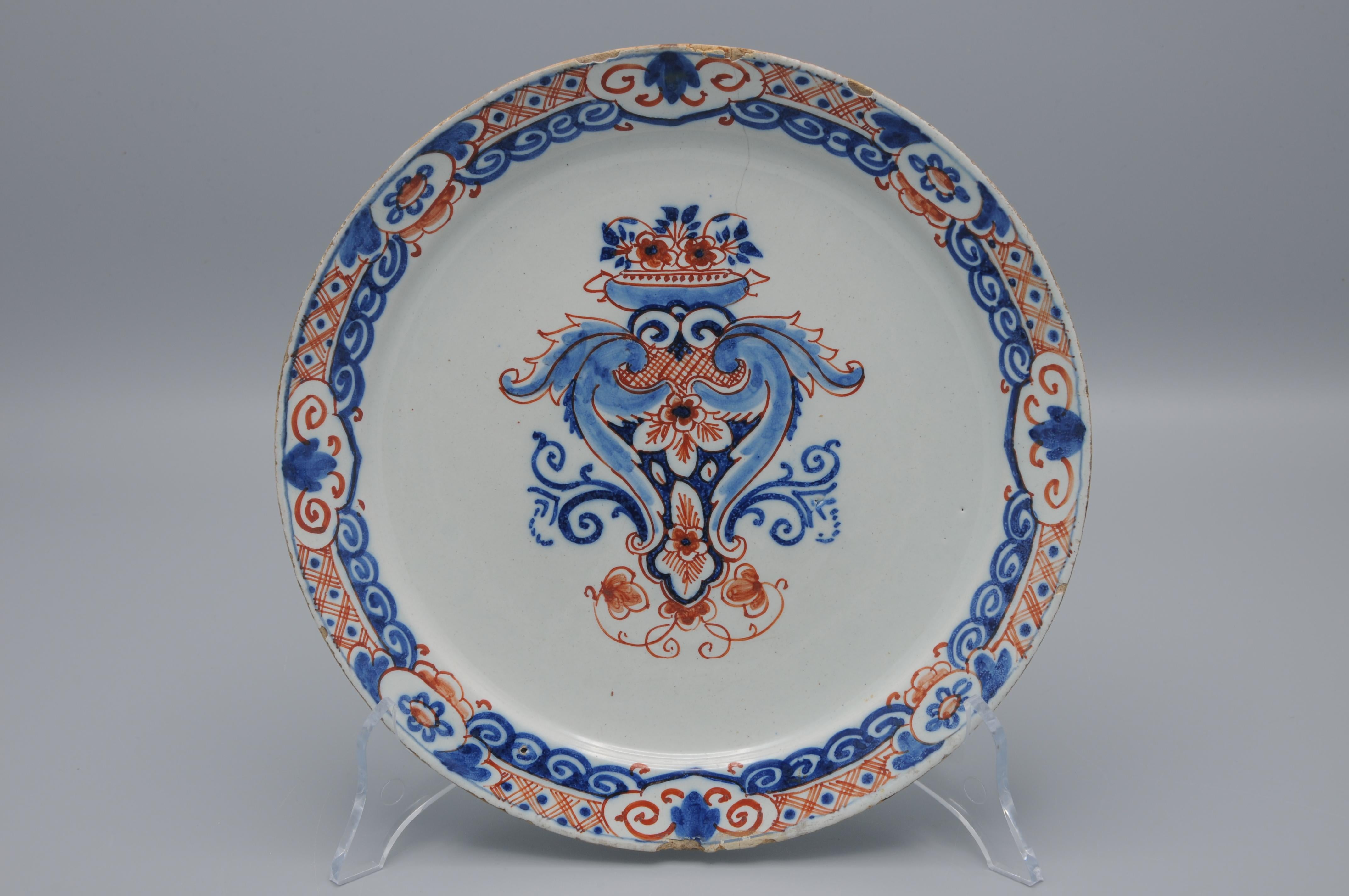 Assiette hollandaise en polychromie de Delft à décor polychrome animé d'une création ornementale centrale Louis XIV couronnée d'un vase sur pied rempli de fleurs. Bordure très ornée avec alternance de cartouches, de traceries et de rinceaux.

Marque