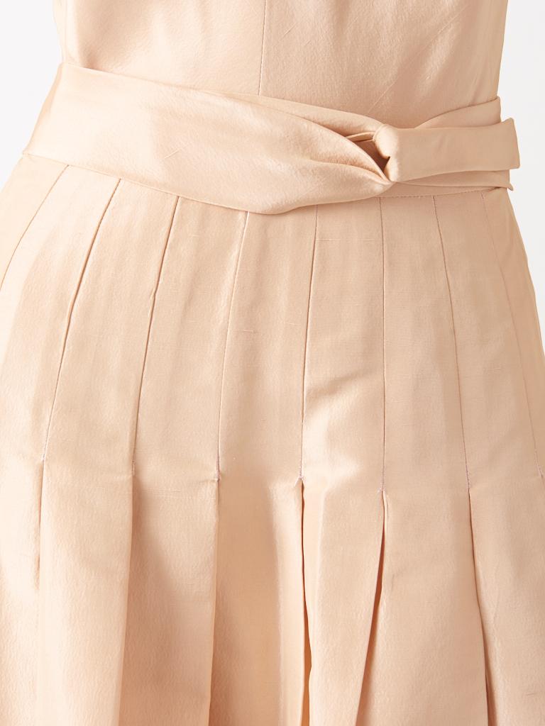 John Anthony, taffeta faille, shell pink tone, halter neck, evening gown, having an open back, deep V in front, with a small stand up pointed collar detail. Skirt is loosely box pleated, having the pleating stitched down at the waist continuing to
