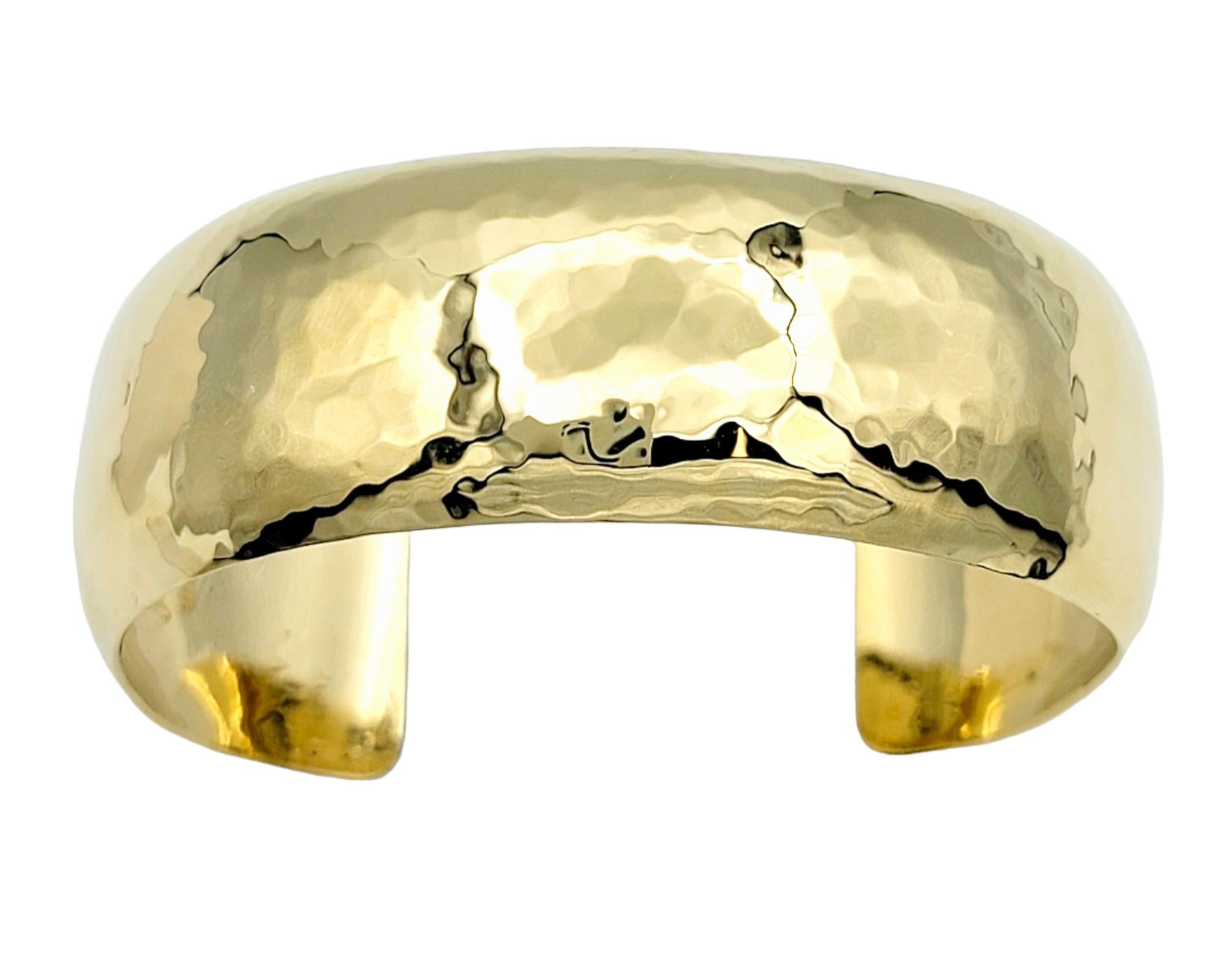 This wide band cuff bracelet, expertly crafted in lustrous 18 karat yellow gold, seamlessly combines versatility with understated elegance. The hammered finish not only adds a touch of textural allure but also contributes to the bracelet's