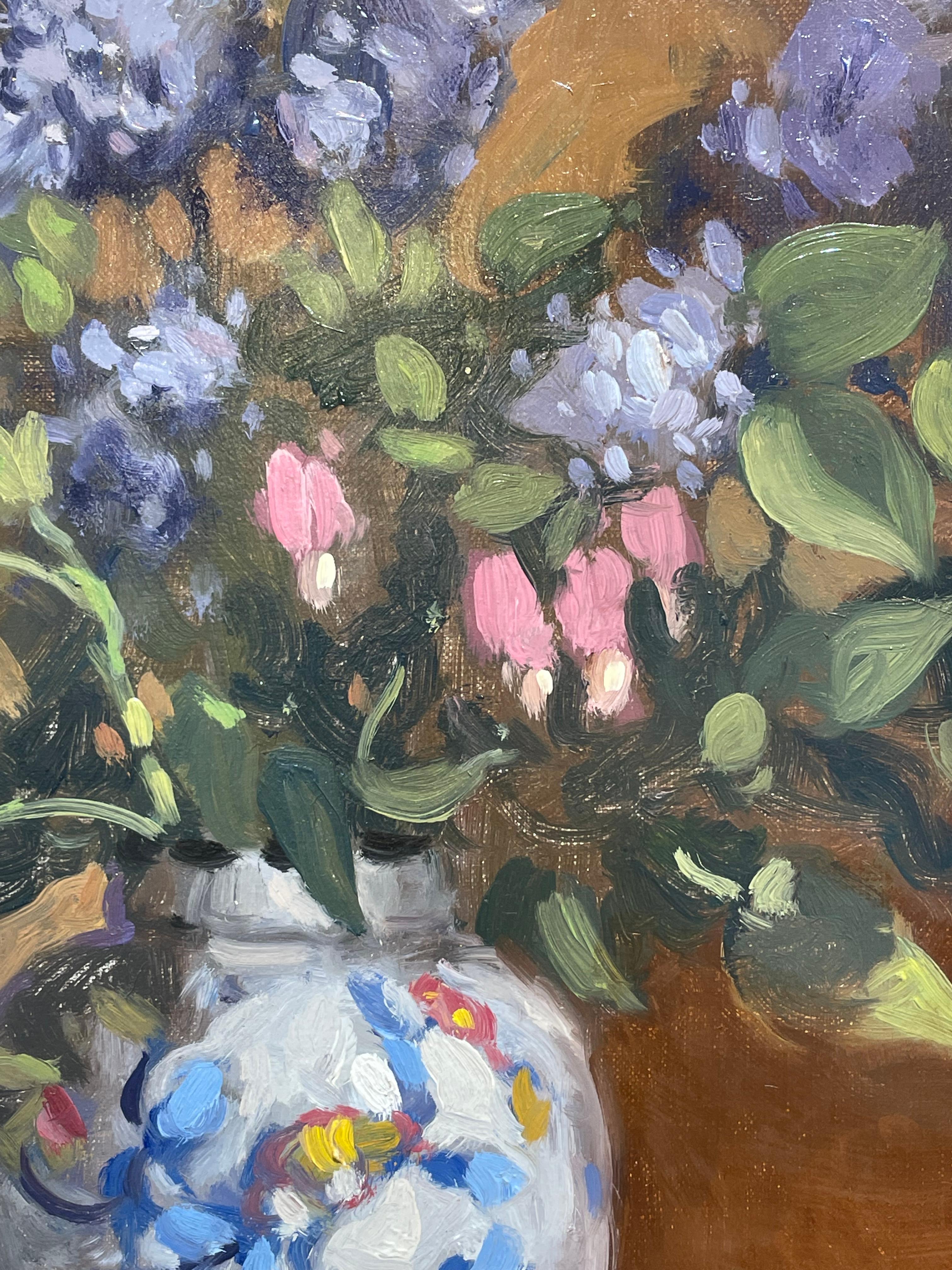 This still life oil painting by John Traynor captures a scene of a large bouquet of purple and pink lilacs in a colorful, porcelain vase. It sits on an off-white fabric next to a lemon which is half peeled, the peel spiraling off the edge of the