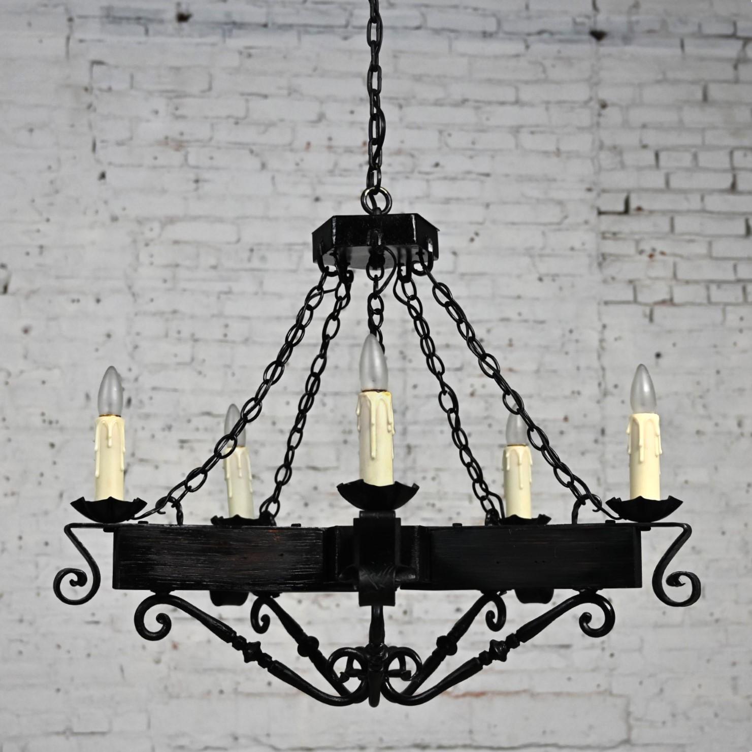 Marvelous vintage John C. Virden Medieval Gothic or Spanish Revival Style Hanging Light Fixture comprised of a 5-arm pentagon shaped black iron and wood fixture, a black iron chain, hammered iron details, candle posts, and a round brass canopy.