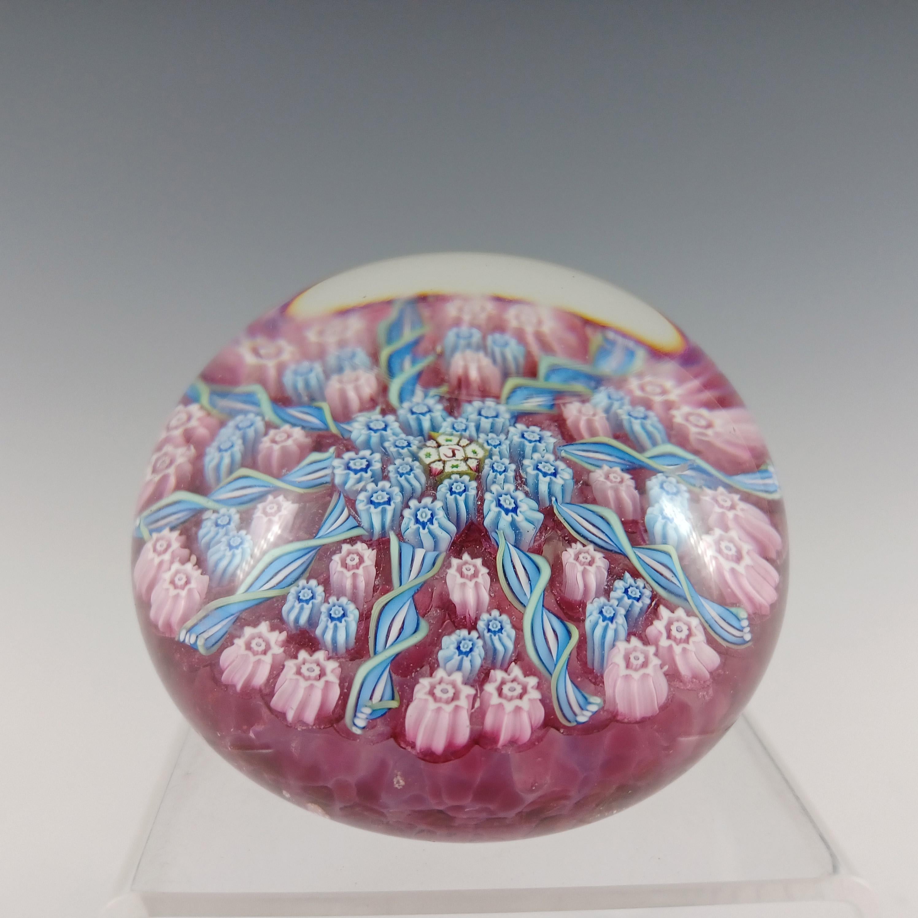 Pisapapeles radial escocés de cristal rosa y transparente relleno de bastones millefiori azules, rosas y blancos. Fabricado por John Deacons, en su fábrica Jay Glass, creada tras dejar Perthshire Glass y antes de fundar John Deacons Glass. Jay Glass