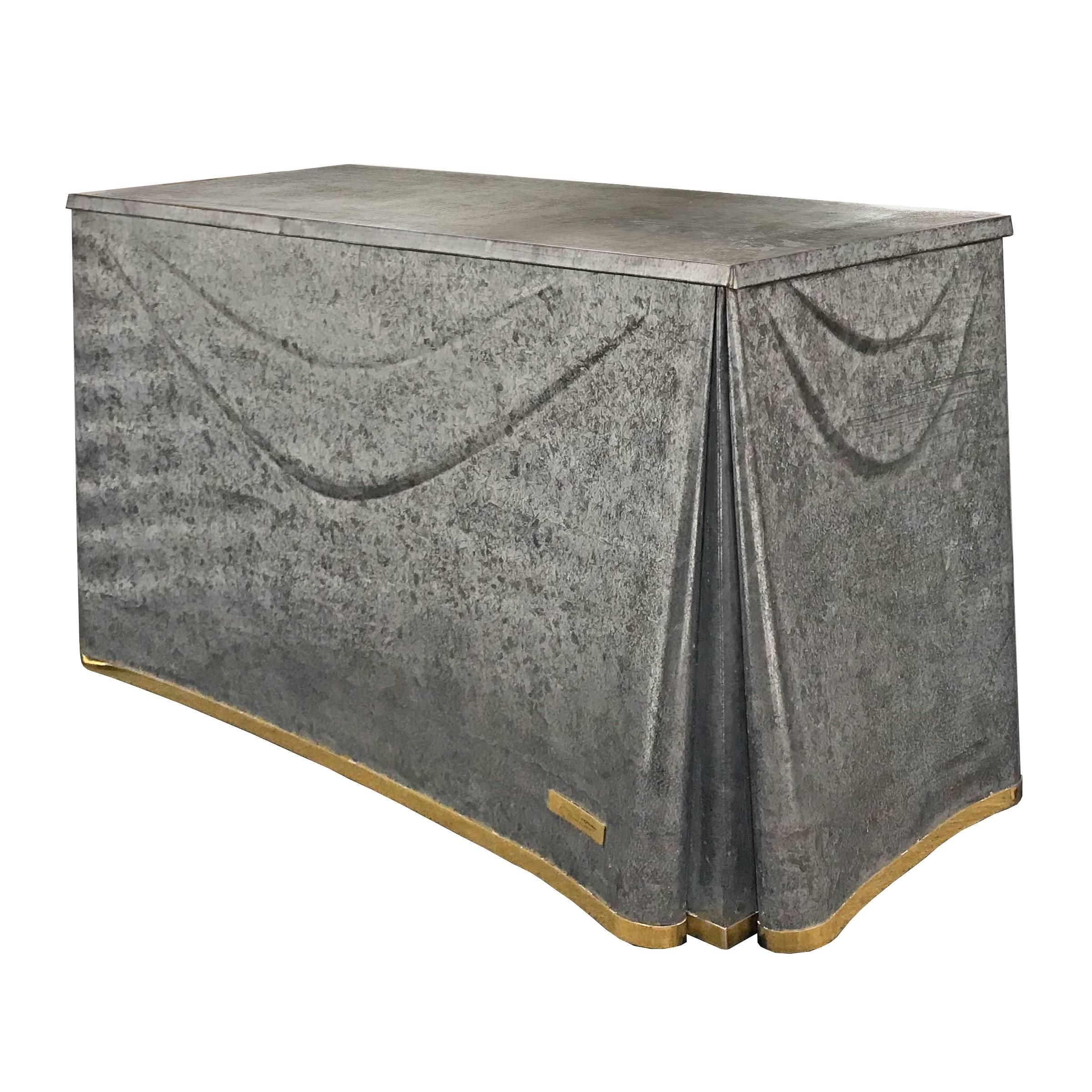 A 21st century reedition John Dickinson galvanized tin console table being of draped cloth form, with brass trim and applied tag reading, 