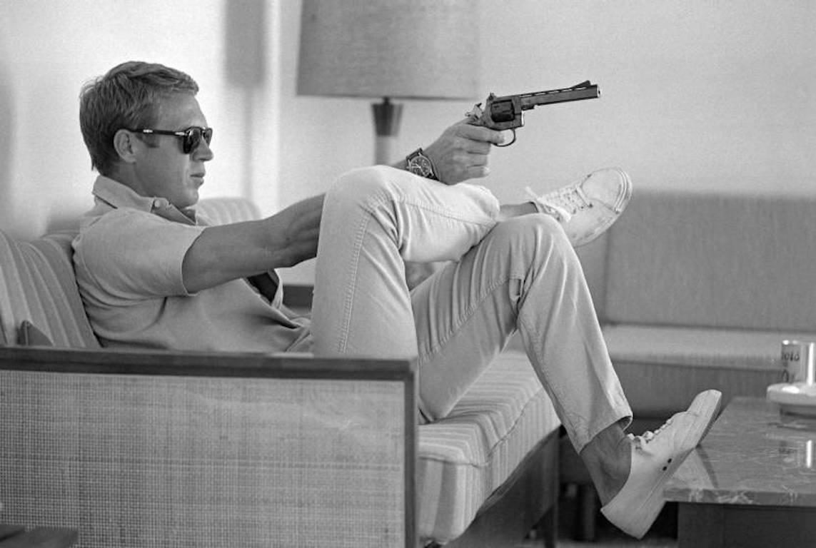 John Dominis Black and White Photograph - Steve McQueen aims a pistol in his living room, California, 1963