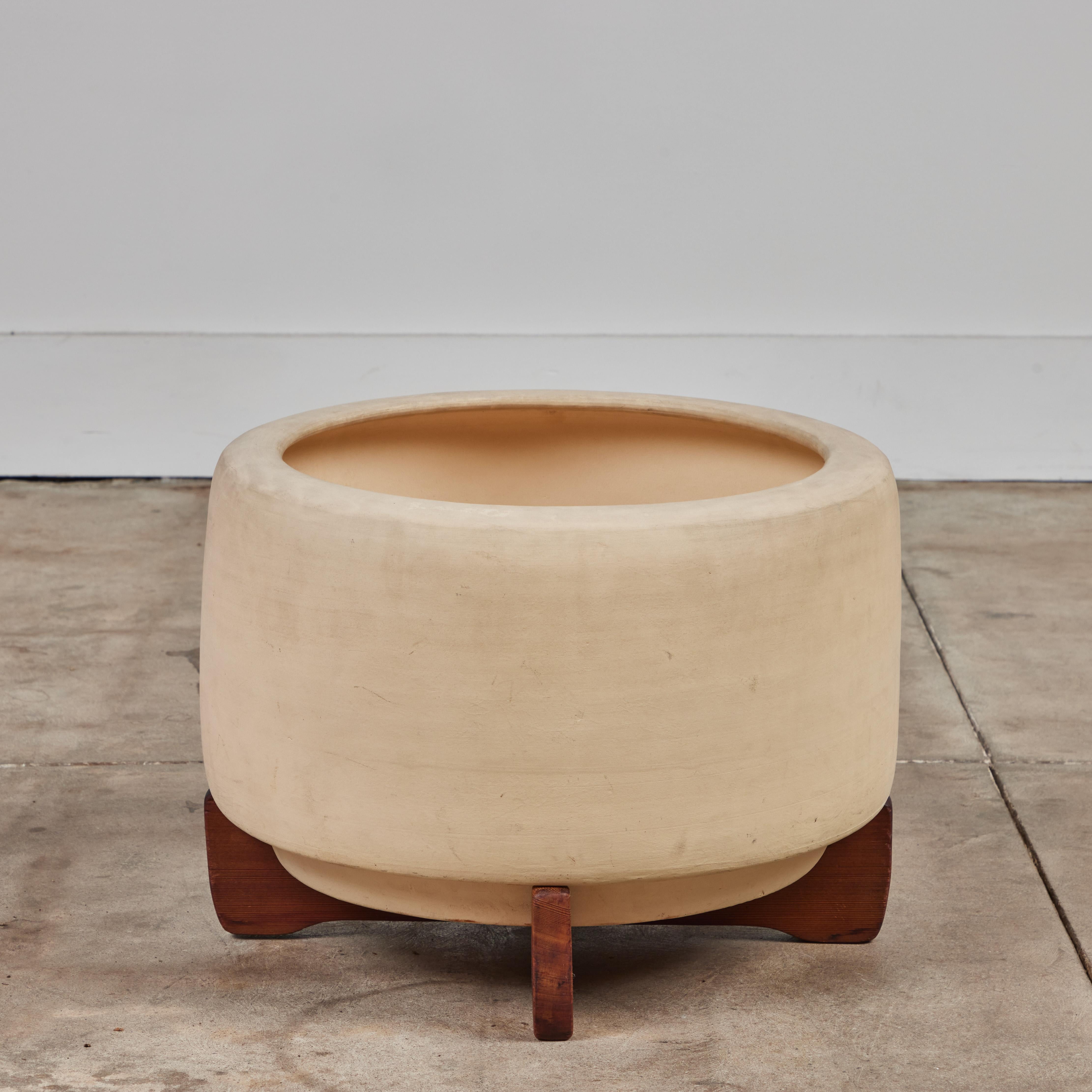 Bisque planter by John Follis for Architectural Pottery. This example has a drum shape with a rounded lip that curves in at the top of the piece. It rests on original wood cross base frame.
Planter is stamped “Architectural Pottery Made in the USA.”
