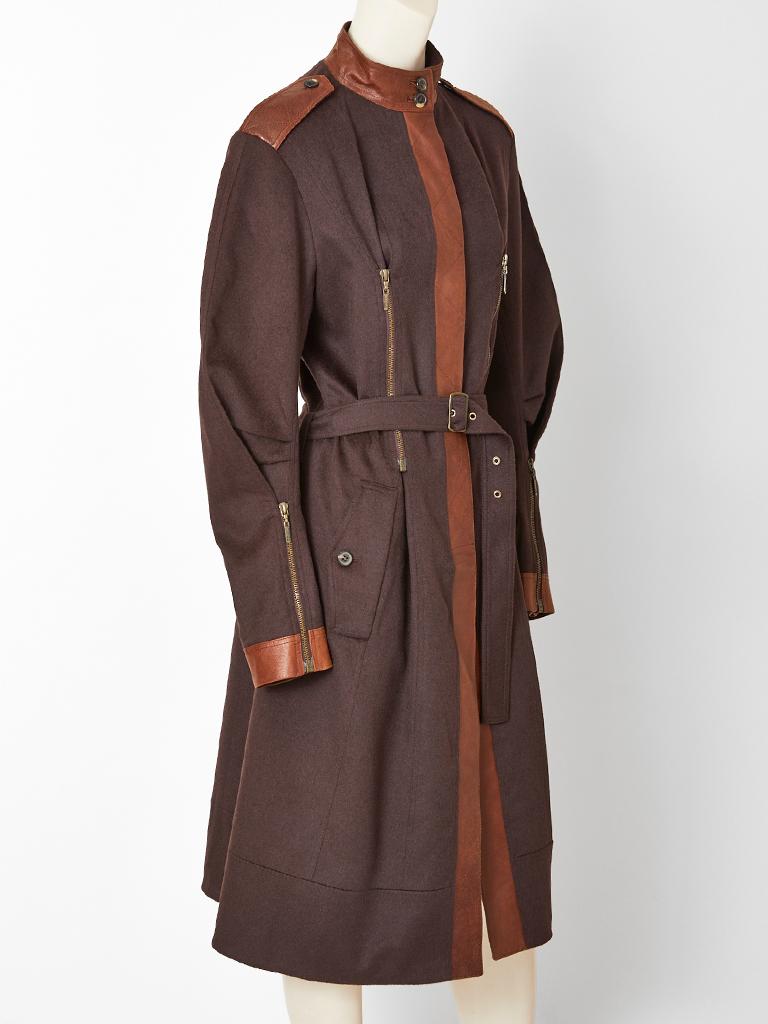 John Galliano, belted, wool coat , having leather detail at the neck, shoulder, center front and cuffs. Coat has no collar, with leather epaulettes. Zipper detail start at the bust darts, going down the bodice. Same zipper detail at the back as