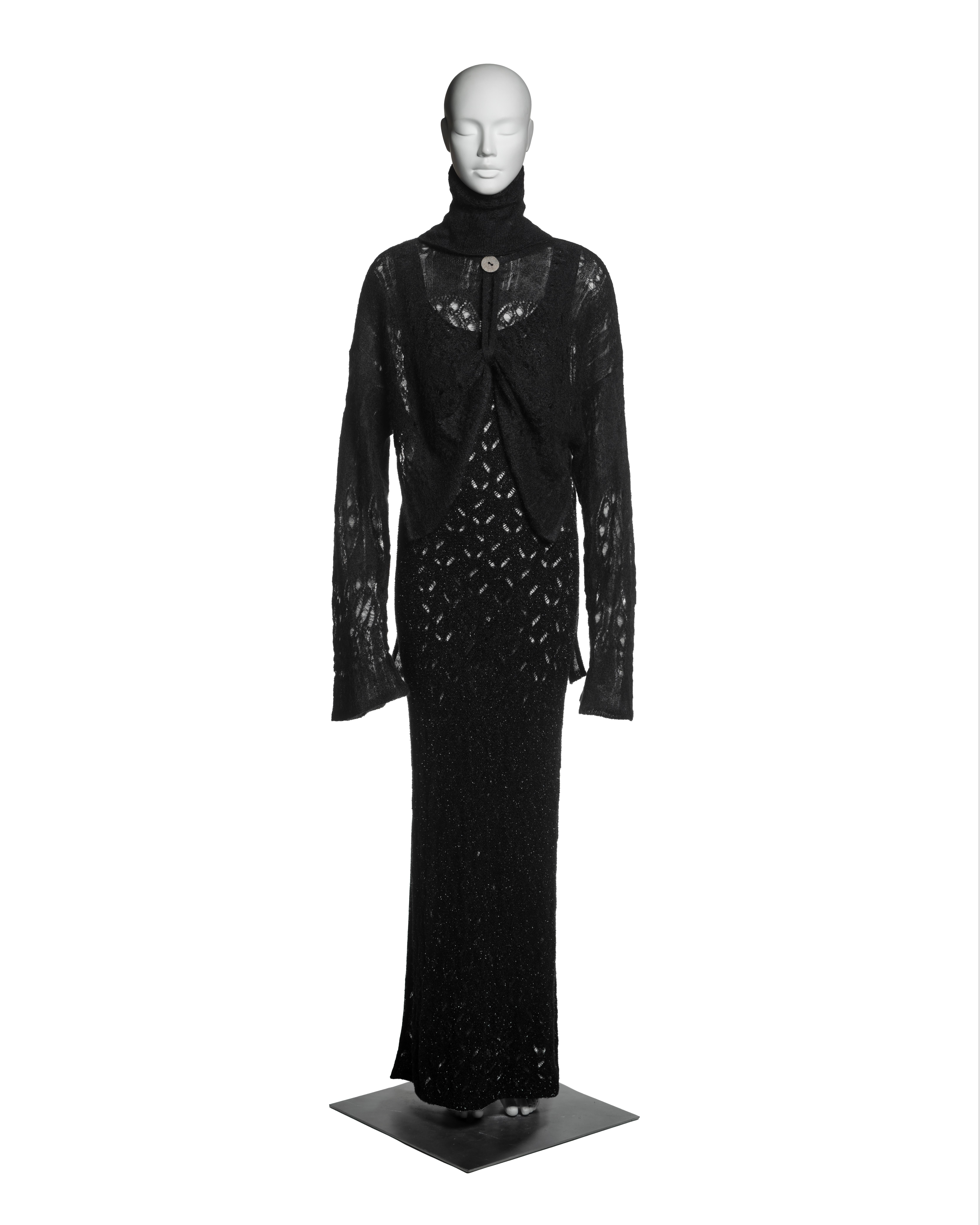 This John Galliano ensemble from the Fall-Winter 2000 collection consists of a full-length dress in a black knitted viscose and nylon blend with metallic yarns interwoven throughout, creating a subtle shimmering effect. Layered over the dress is a
