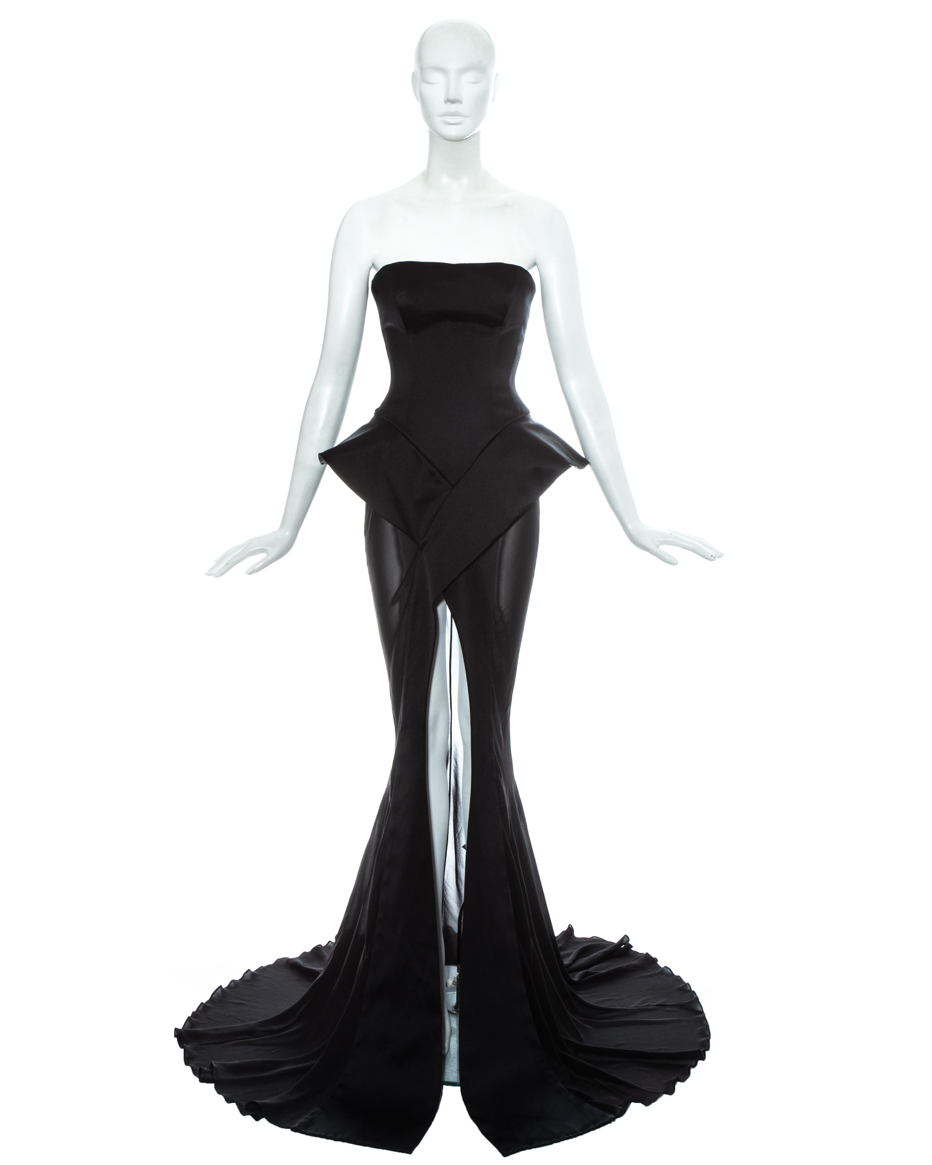 John Galliano; black silk strapless evening gown. 

- Boned bodice with built-in corset and accentuated v-shaped waist. 
- Large peplum forming a criss cross to the front of the bias-cut multi-panelled trained chiffon skirt with high leg slit. 
- 30