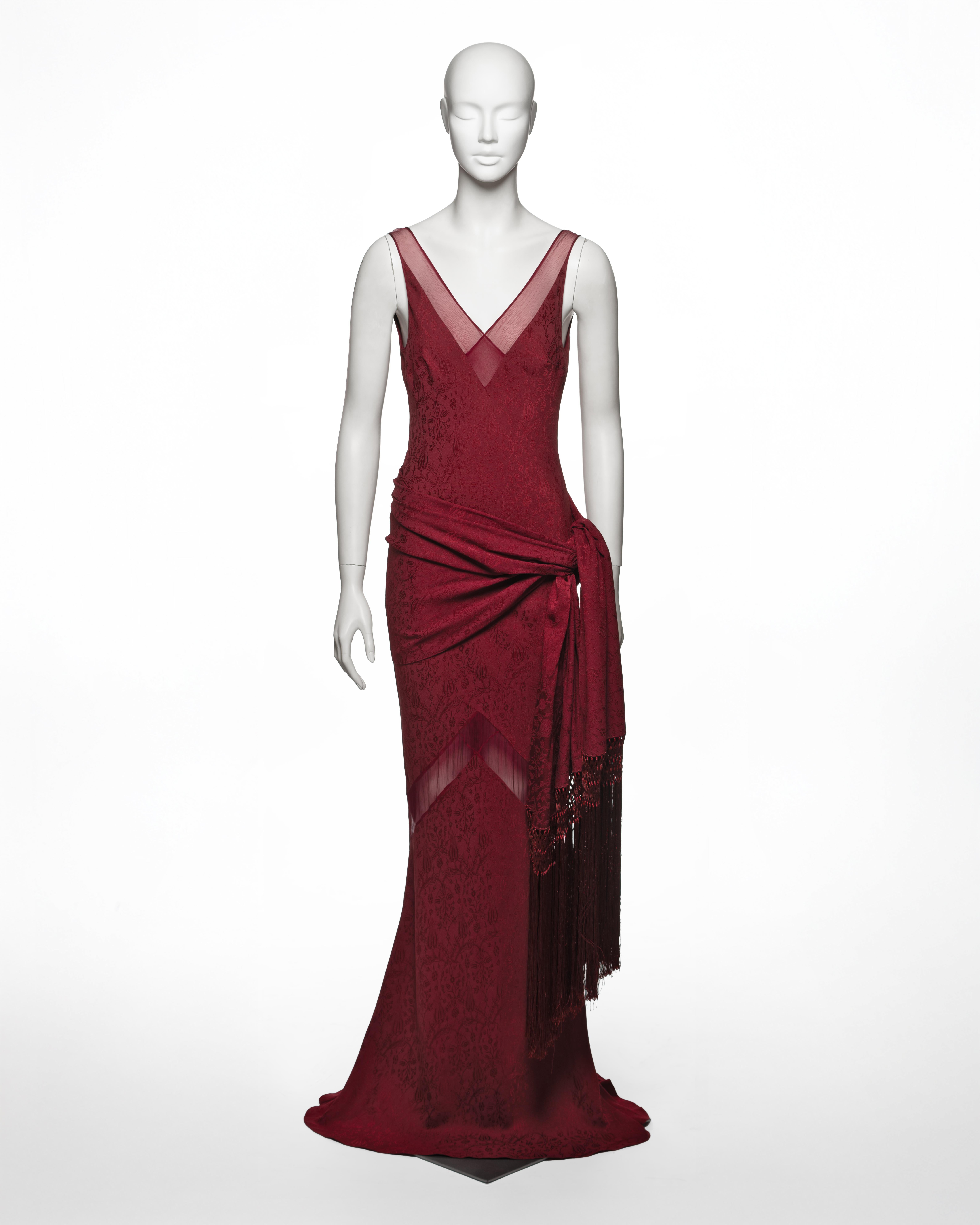 Cet ensemble du soir John Galliano de la collection printemps-été 1999 se compose d'une robe longue en biais et d'un châle assorti, réalisés en damas bordeaux foncé avec des motifs floraux ton sur ton et des empiècements en mousseline de soie