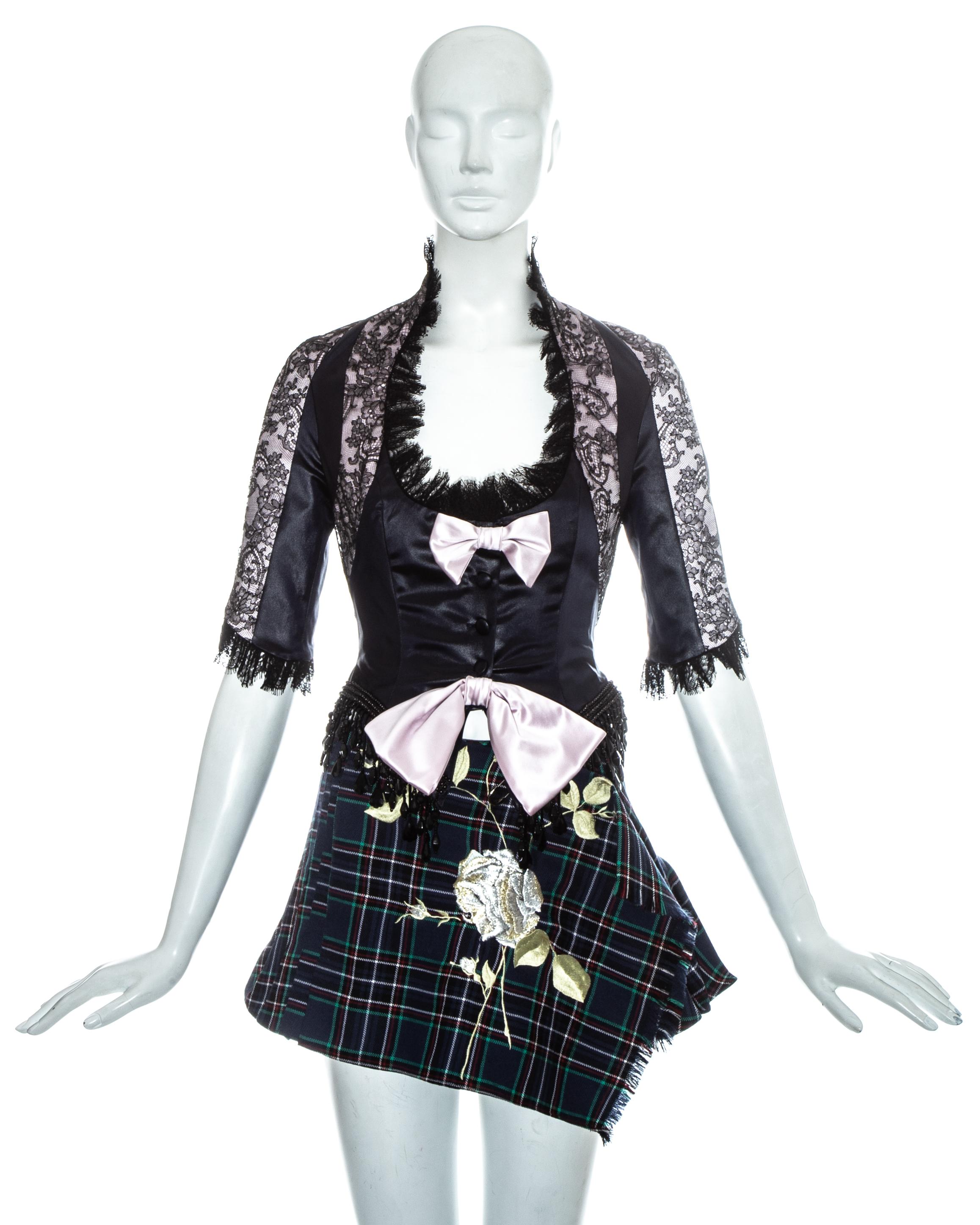 Ensemble de défilé John Galliano. Corset à panneaux en dentelle et satin rose avec garniture de franges en dentelle et perles:: deux nœuds décoratifs roses et fermetures à boutons en tissu.  Mini-jupe portefeuille en laine écossaise bleue avec plis