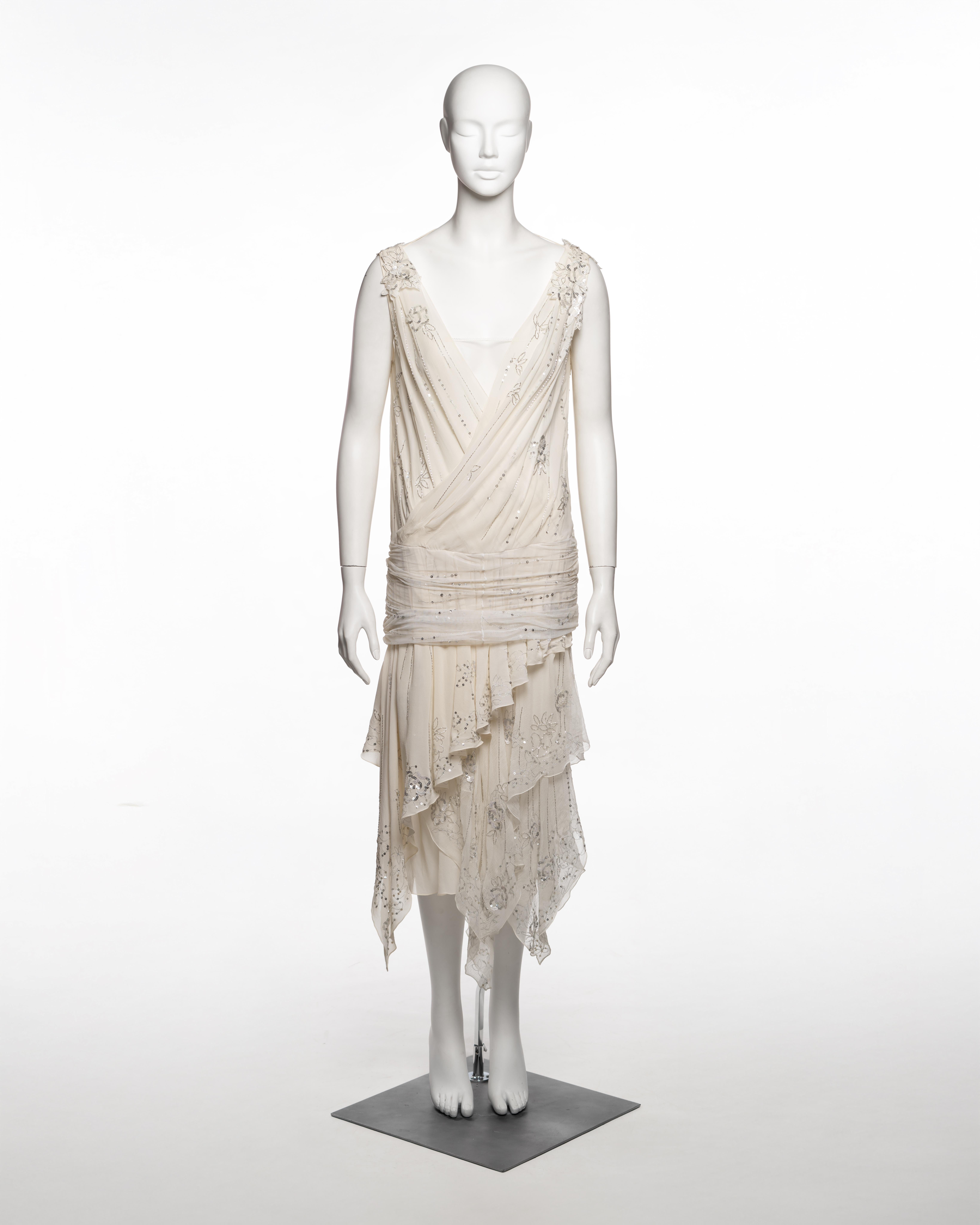 Kleid von John Galliano, Frühjahr-Sommer 2006, aus elfenbeinfarbenem Seidenchiffon in Lagen mit integriertem Unterkleid aus Netzstoff und einem gerüschten Chiffon-Taillenband, das die Hüften bedeckt. Das ärmellose Mieder besteht aus diagonal